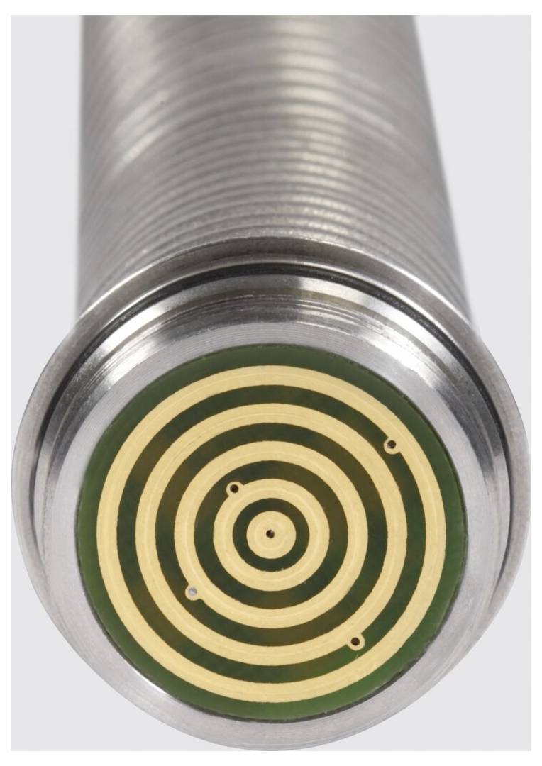 Eine Nahaufnahme eines zylindrischen Metallsensors mit einem konzentrischen kreisförmigen Muster auf seiner Oberfläche, möglicherweise zum Erkennen oder Messen von Eigenschaften.