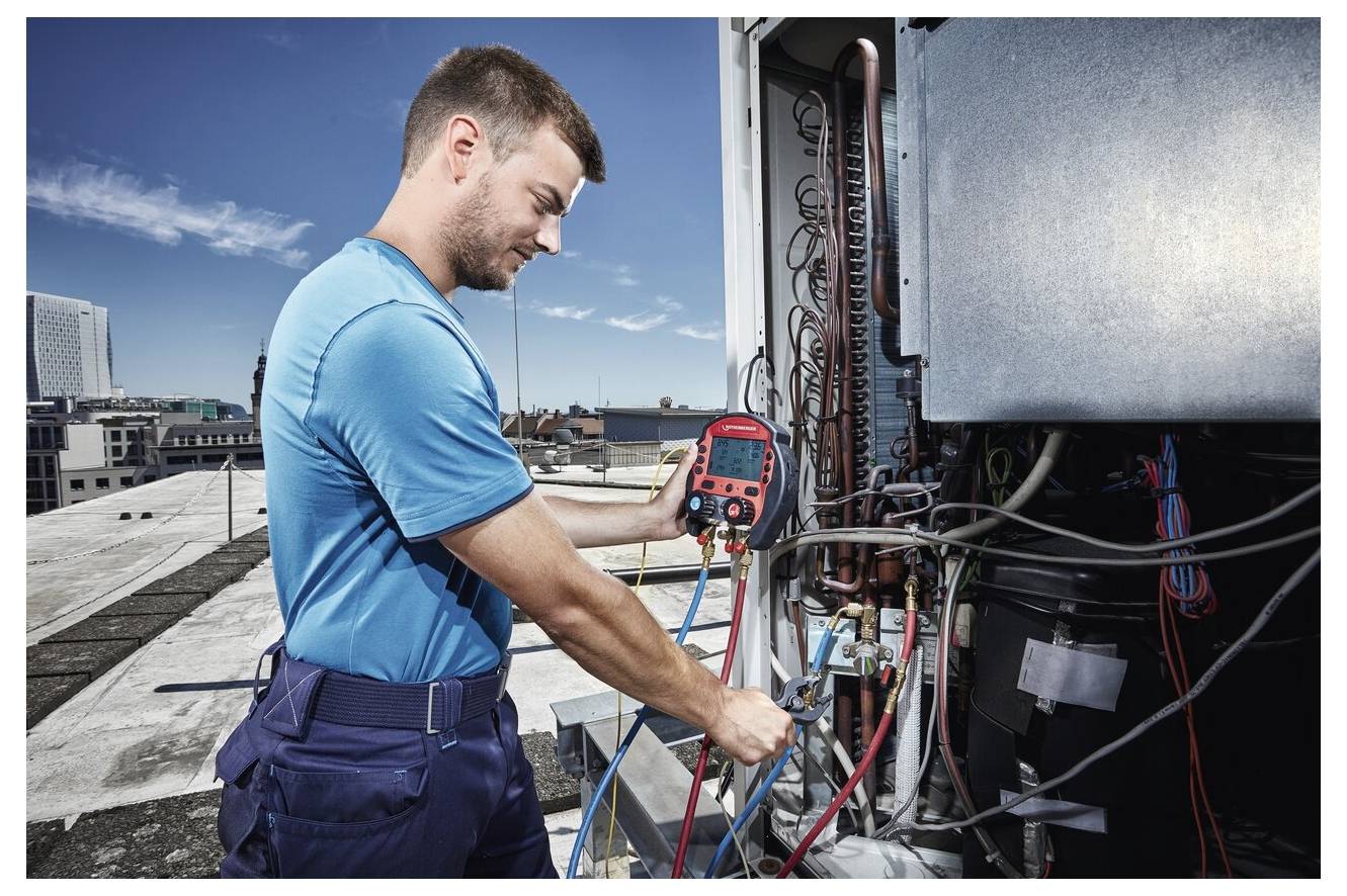 Ein Techniker auf einem Dach nutzt Diagnosegeräte, um eine HVAC-Anlage zu überprüfen, wobei er Druckniveaus und Systemverbindungen bei sonnigem Himmel kontrolliert.