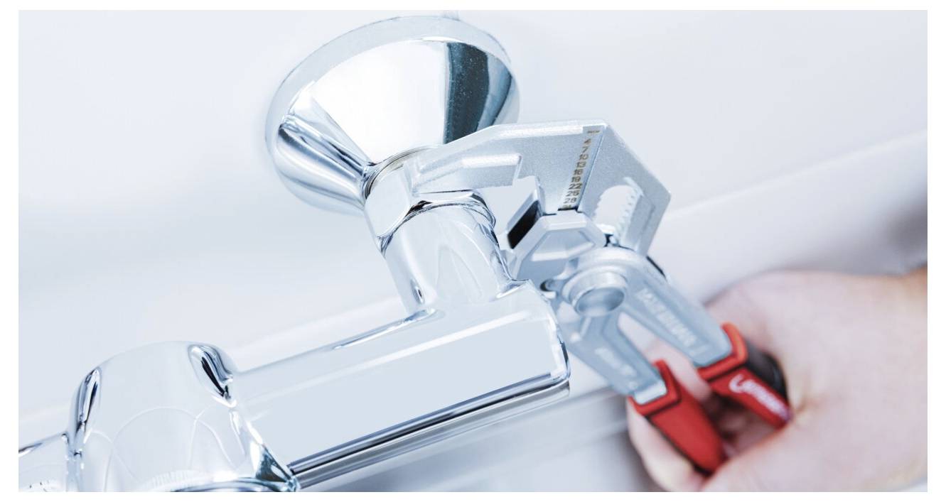 Eine Person benutzt einen Schraubenschlüssel, um einen glänzenden Chromhahn festzuziehen, was Sanitär- oder Reparaturarbeiten im Gange zeigt.