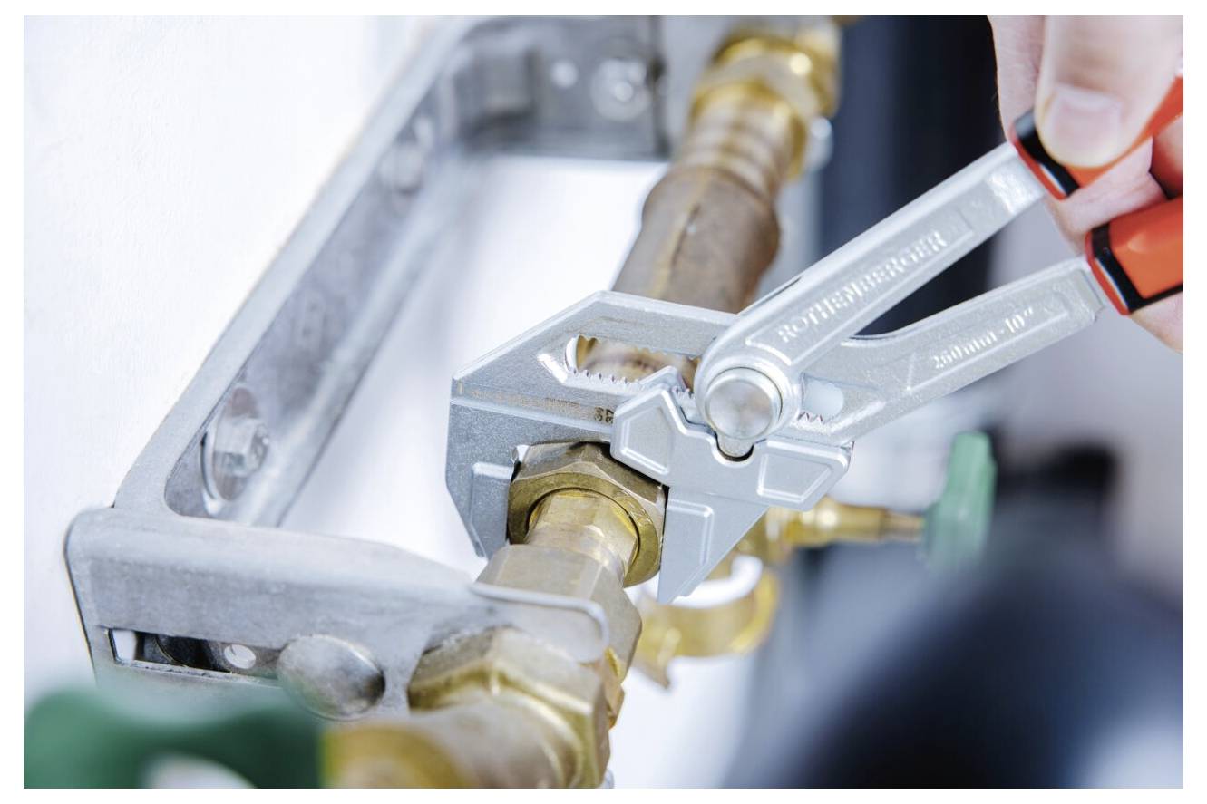 Eine Hand benutzt einen Schraubenschlüssel, um ein Ventil an einem Messingrohr zu festigen, was auf eine laufende Rohrreparatur hindeutet.