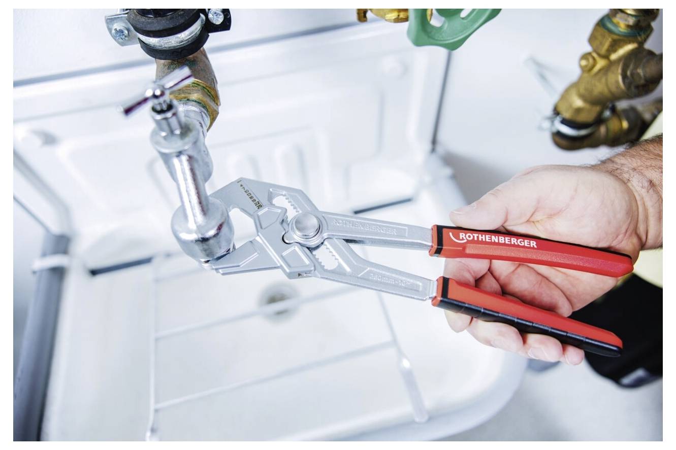 Eine Hand, die mit einer Zange eine Rohrleitung unter einem Waschbecken einstellt und damit Sanitärwartung oder -reparatur veranschaulicht.