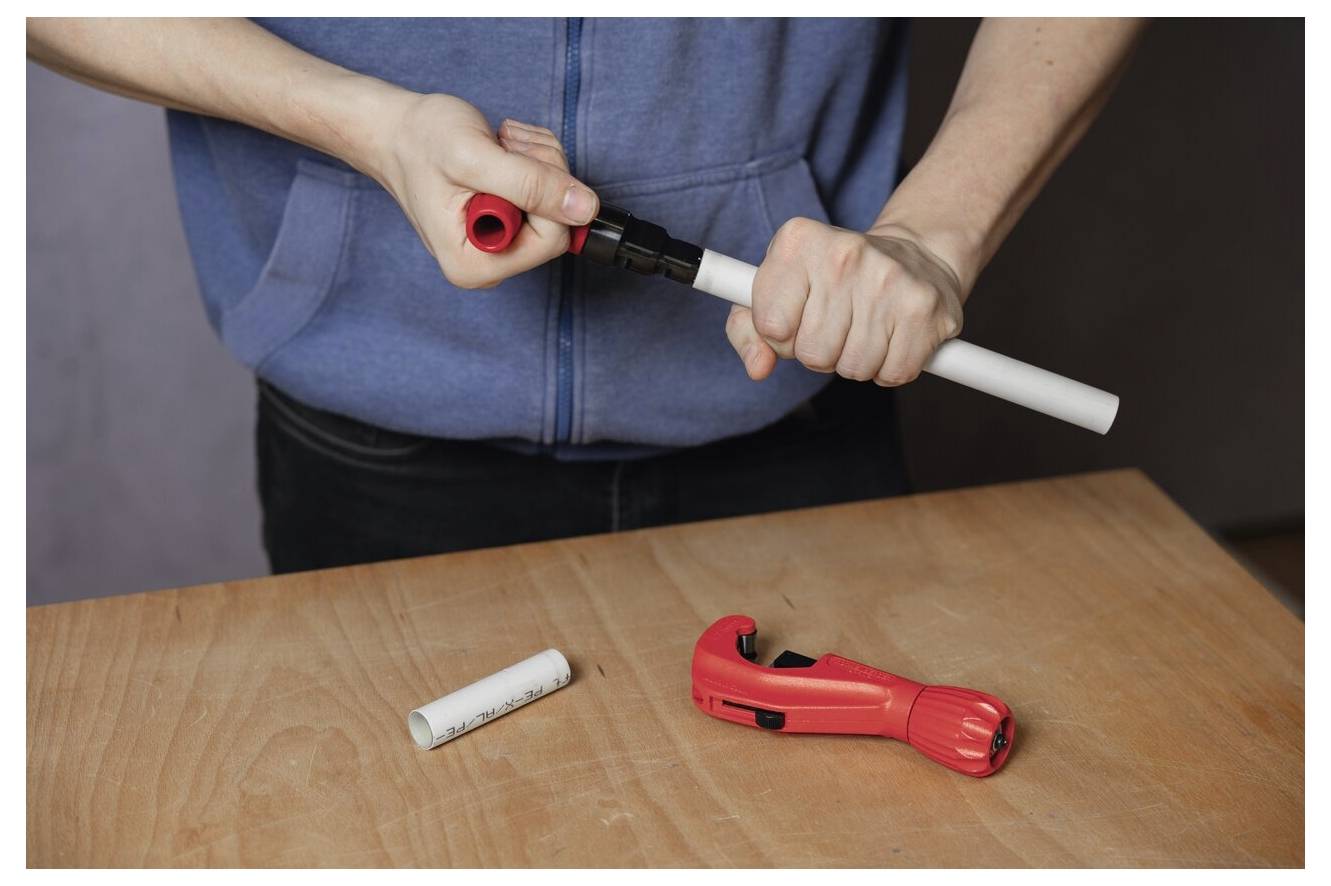 Person in blauem Sweatshirt, die ein Werkzeug verwendet, um PVC-Rohre auf einem Holztisch zu verbinden, mit einem Rohrabschneider in der Nähe.