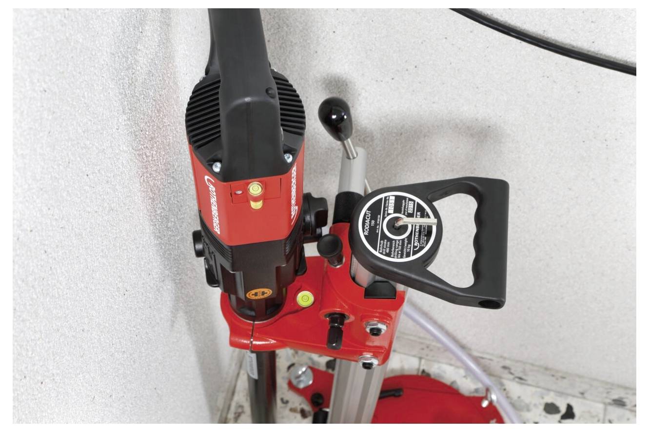 Eine rote und schwarze Standbohrmaschine, die auf einem vertikalen Ständer montiert ist, wird an einer Wand stehend gezeigt.