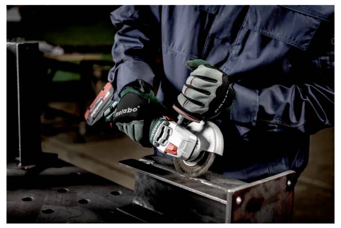 Eine Person in Arbeitskleidung verwendet eine tragbare Elektrowinkelschleifer auf einer Metalloberfläche und präsentiert dabei industrielle Ausrüstung und Handwerkskunst.