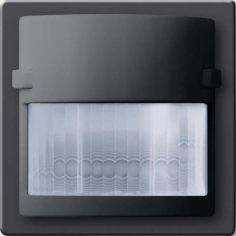 Ein schwarzer Bewegungsmelder mit rechteckigem Design und einer klaren, strukturierten Linse. Er ist auf einer dunklen Oberfläche montiert.