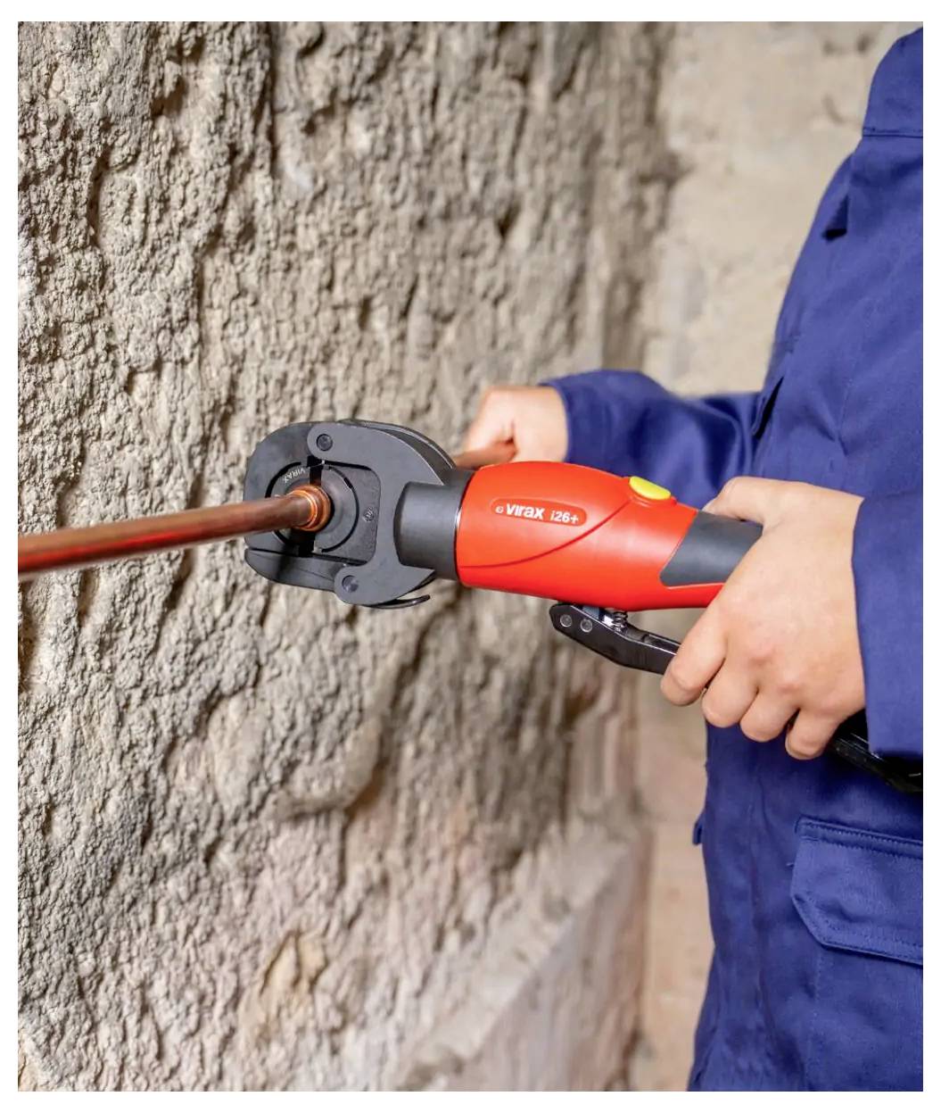 Arbeiter, der ein rotes Rohrzange auf ein Kupferrohr gegen eine raue Wand verwendet.