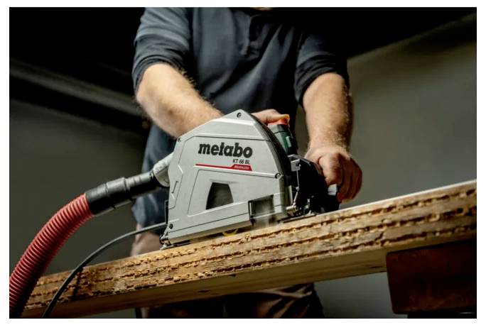 Person, die eine Metabo-Kreissäge zum Schneiden eines Holzbretts verwendet, mit angeschlossenem Staubschlauch.