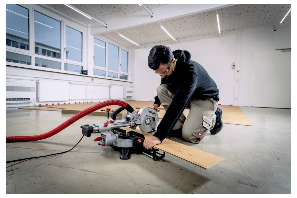 Eine Person, die mit einer Kreissäge Holzbretter in einem geräumigen, hell erleuchteten Raum schneidet und dabei Schutzbrille und Gehörschutz zum Eigenschutz trägt.
