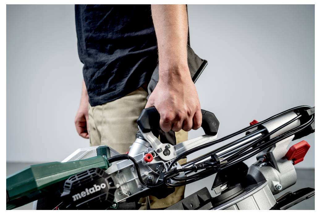 Eine Person, die den Griff eines Elektrowerkzeugs, möglicherweise einer Säge, in Gebrauchsposition hält. Das Werkzeug enthält einen grünen Abschnitt mit der Beschriftung 