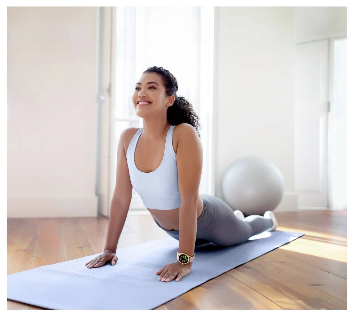 Eine Frau in Sportkleidung praktiziert Yoga auf einer Matte und macht eine Kobra-Pose in einem sonnendurchfluteten Raum mit einem Gymnastikball im Hintergrund.
