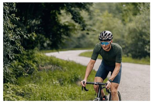 Eine Person in Radsportbekleidung fährt ein Fahrrad auf einer kurvenreichen Straße durch einen üppigen, grünen Wald.