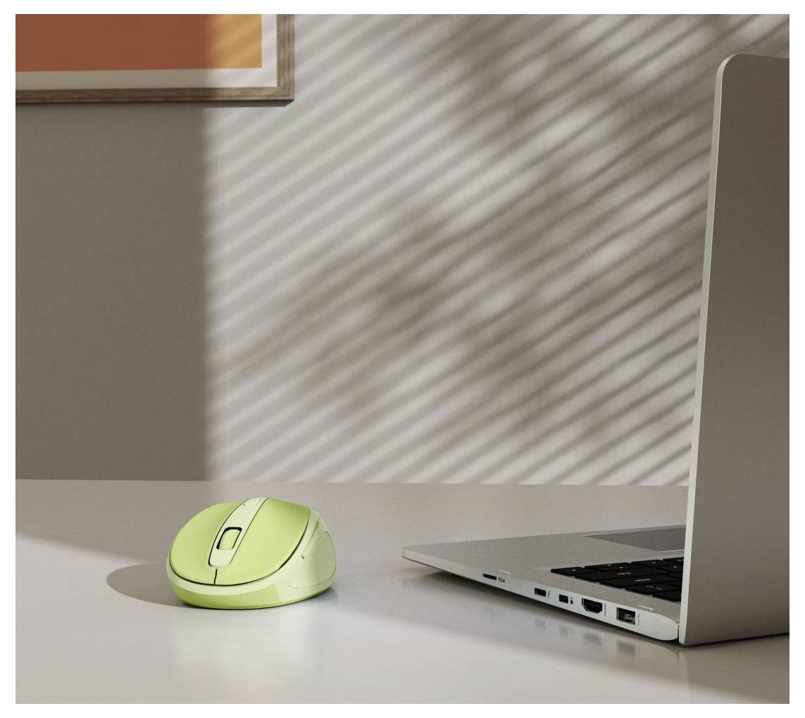 Eine grüne kabellose Maus auf einem Schreibtisch neben einem silbernen Laptop, wobei das Sonnenlicht gestreifte Schatten erzeugt.