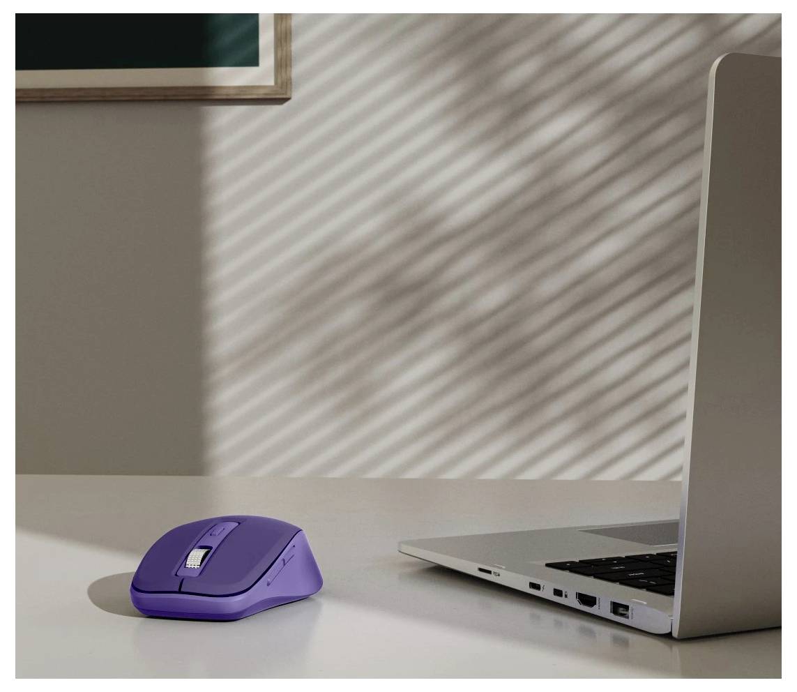 Eine lila kabellose Maus auf einem weißen Schreibtisch neben einem silbernen Laptop. Sonnenlicht wirft Schatten der Jalousien an der Wand im Hintergrund.