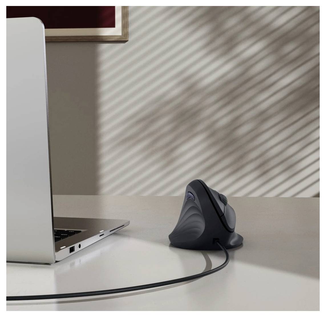 Ein Laptop auf einem Schreibtisch neben einer vertikalen ergonomischen Maus. Sonnenlicht erzeugt gestreifte Schatten an der Wand und erhöht die Atmosphäre des Arbeitsplatzes.