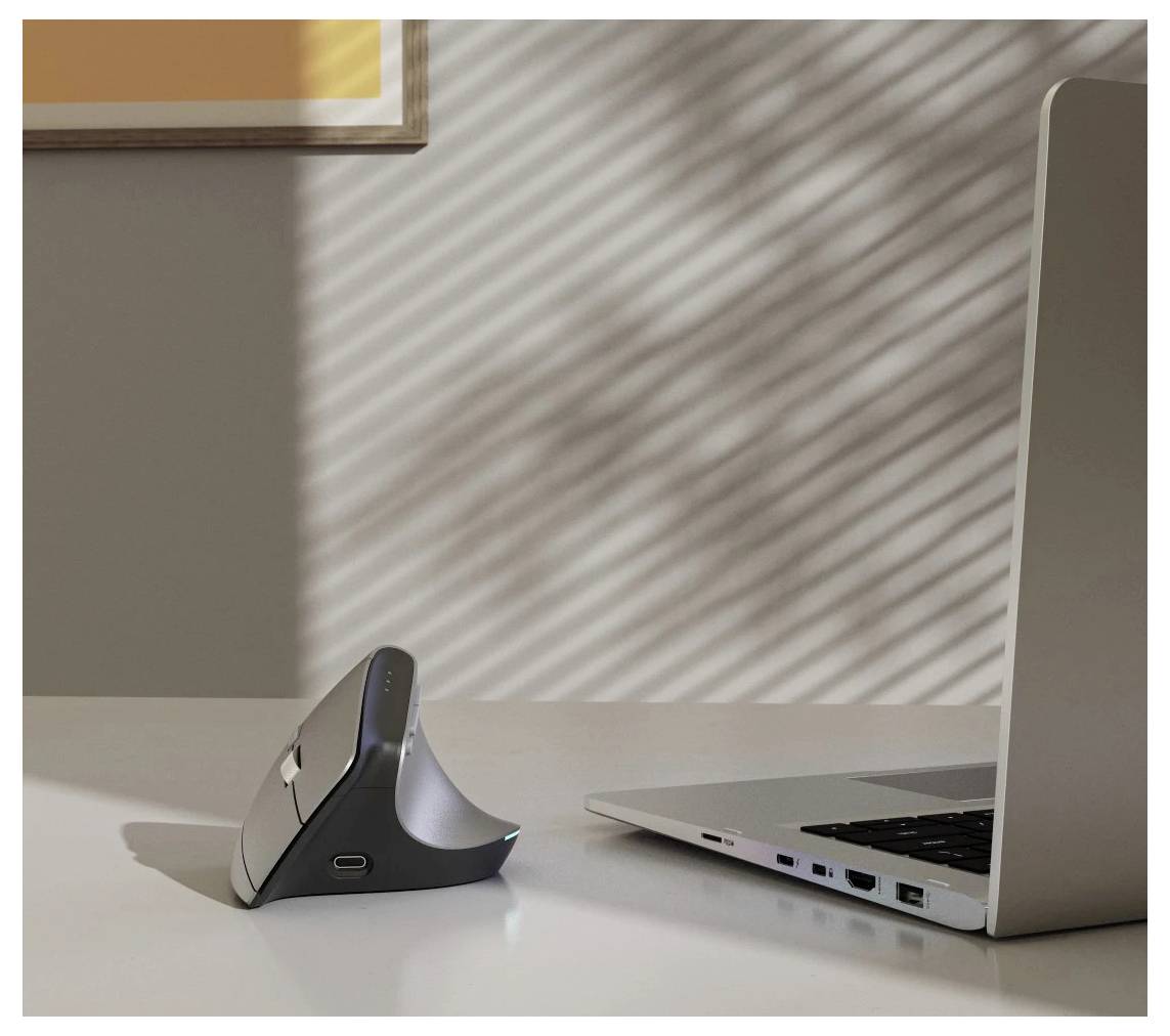 Eine schlanke, kabellose vertikale Computermaus auf einem Schreibtisch neben einem silbernen Laptop unter weichem, gefiltertem Licht von Jalousien.