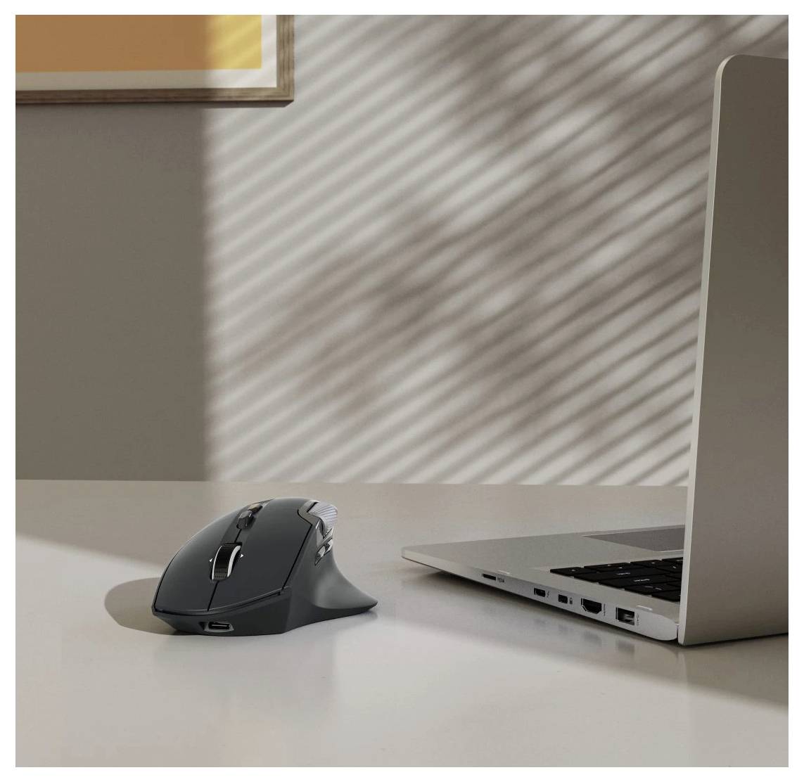 Eine kabellose Maus neben einem geöffneten Laptop auf einem Schreibtisch, wobei Sonnenlicht gestreifte Muster an der Wand und auf der Oberfläche erzeugt.