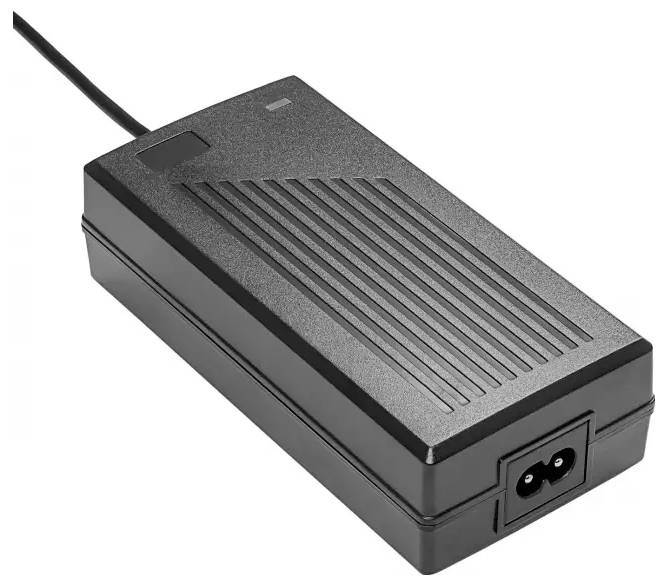 Ein schwarzer Netzadapter, der flach auf einer Oberfläche liegt, mit einem Kabel, das oben herausragt. Er hat eine rechteckige Form und eine geriffelte Textur.