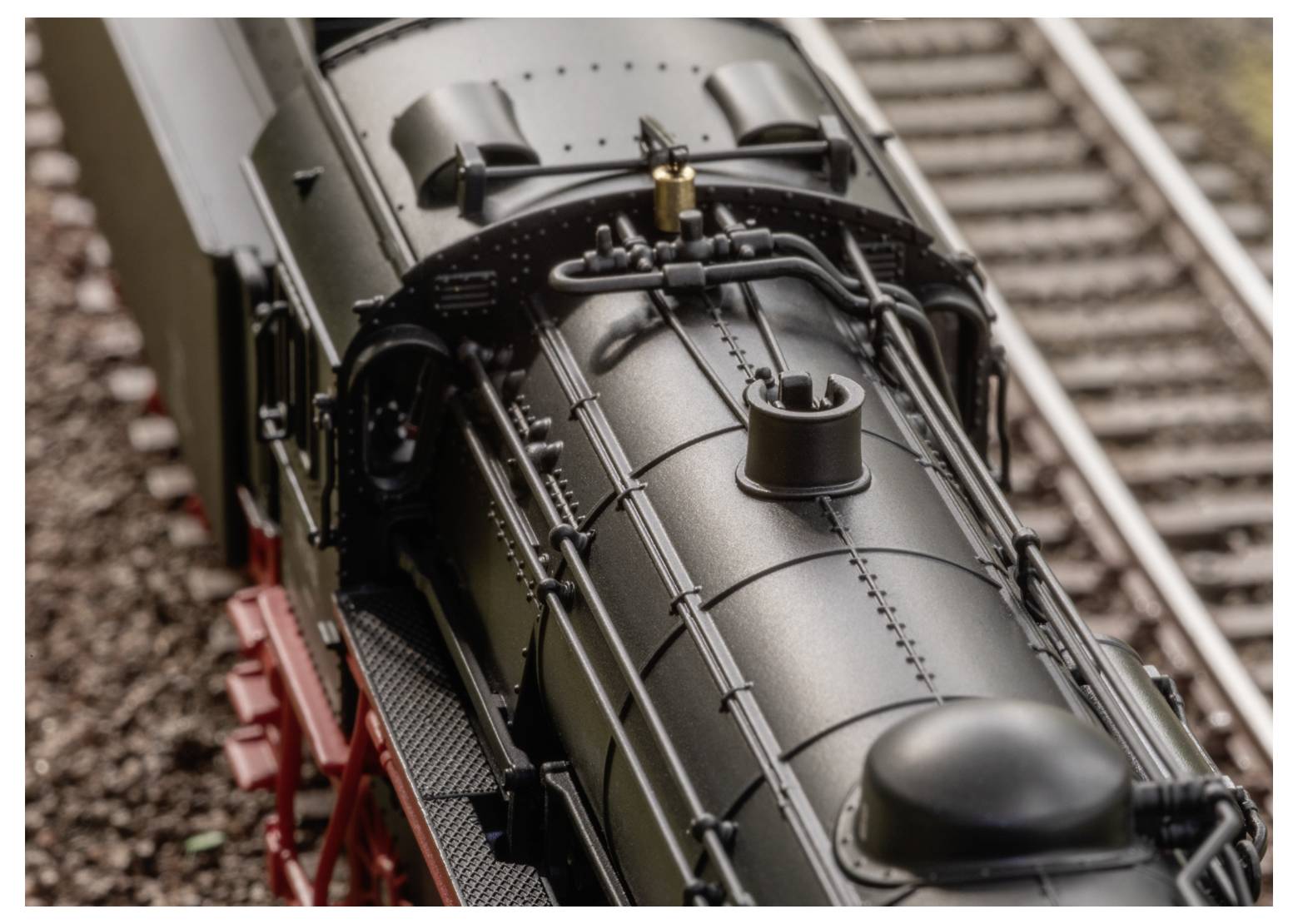 Eine Nahaufnahme einer Modell-Dampflokomotive auf Schienen, die detaillierte Technik mit sichtbaren Rohren und Strukturen auf dem Dach des Zuges präsentiert.