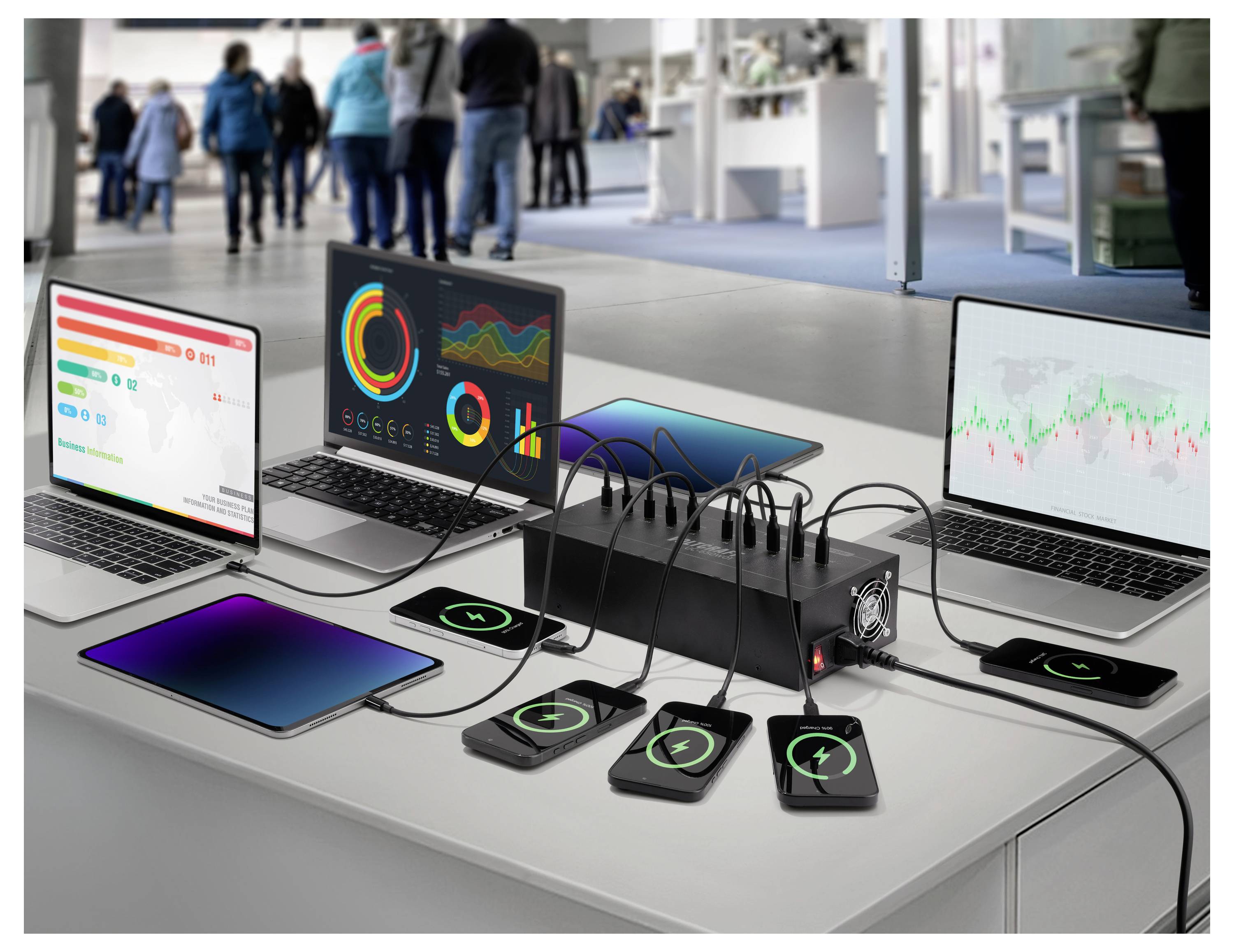 Drei Laptops zeigen Diagramme und Grafiken an. Telefone laden drahtlos auf einem Tisch mit einem Mehrgrätelladegerät auf. Unscharfe Figuren im Hintergrund.