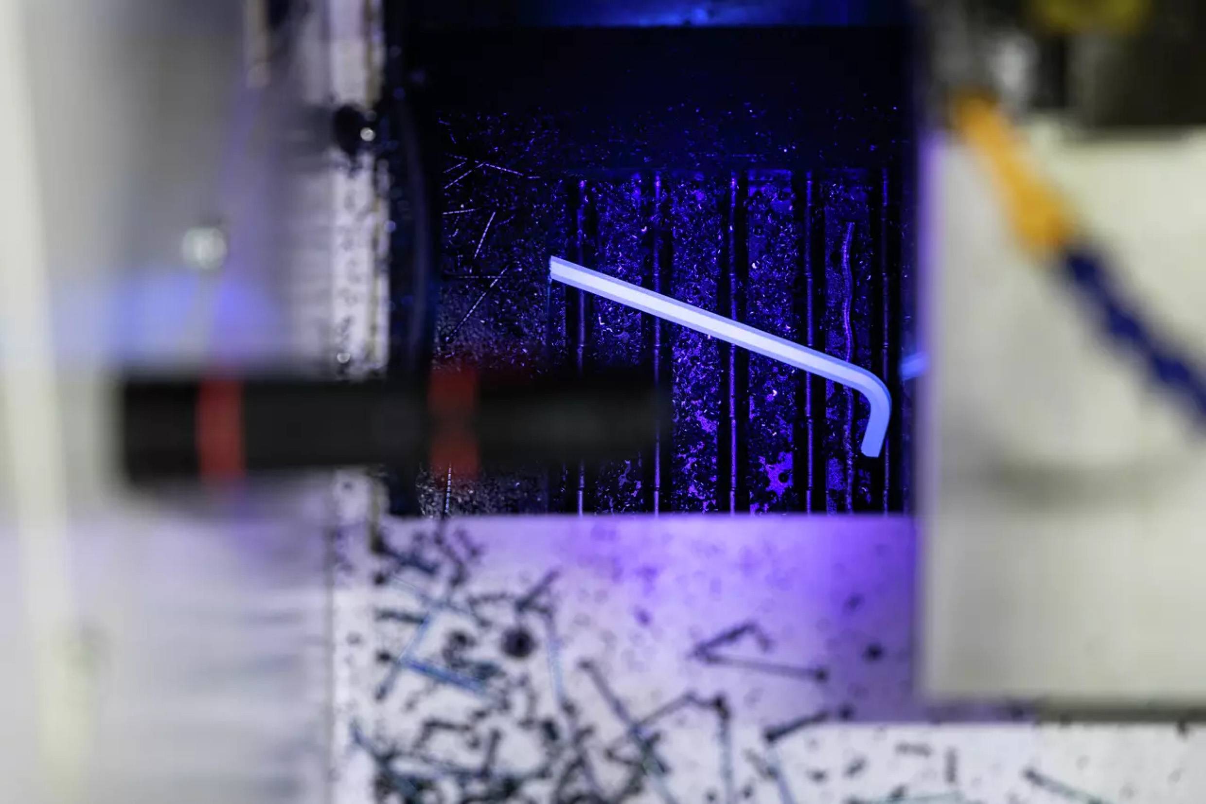 Eine Nahaufnahme eines weißen Objekts vor einem dunklen industriellen Hintergrund mit verstreutem Trümmerwerk und violetter Beleuchtung, möglicherweise in einer Fertigungsumgebung.