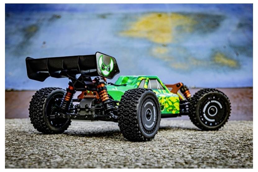 Ein grünes und schwarzes ferngesteuertes Auto mit großen Reifen und einem Spoiler, auf einer strukturierten Oberfläche, mit blauer Wand im Hintergrund.