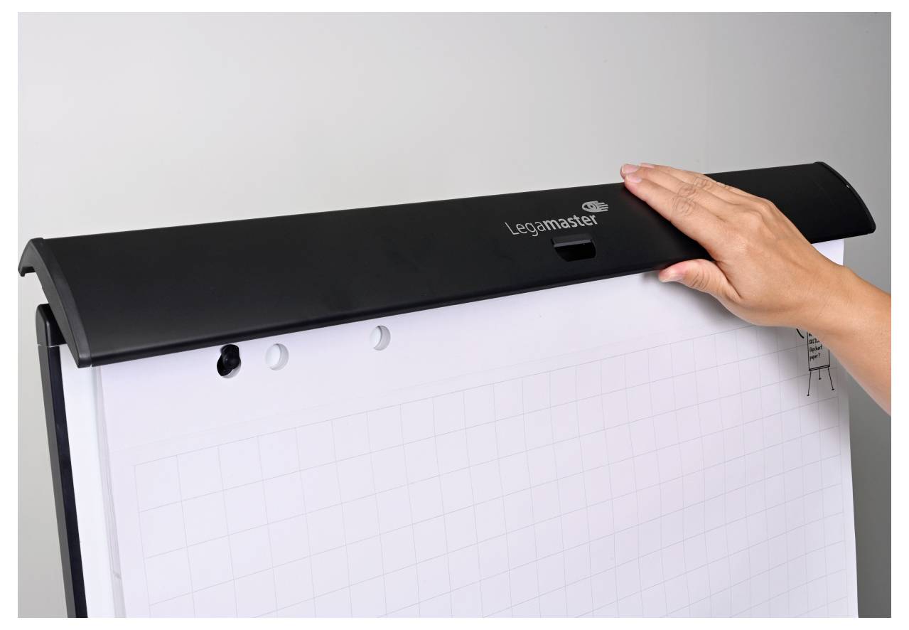 Eine Hand justiert einen schwarzen Clip an der Spitze eines Flipchart-Ständers, der Graphenpapier hält und für Präsentationen oder Besprechungen verwendet wird.