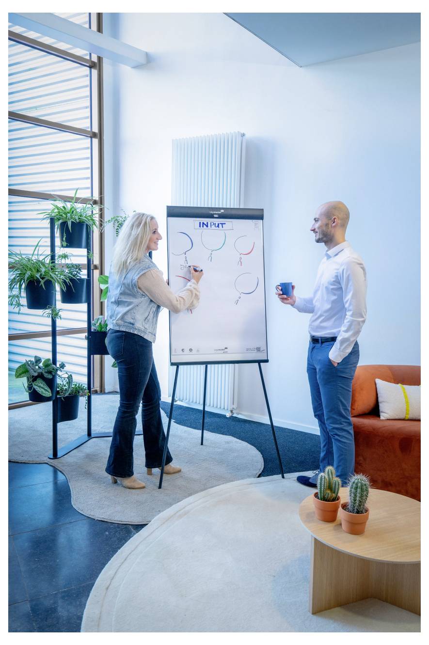 Eine Frau und ein Mann diskutieren in einem Büroumfeld, während die Frau auf ein Whiteboard mit der Beschriftung 