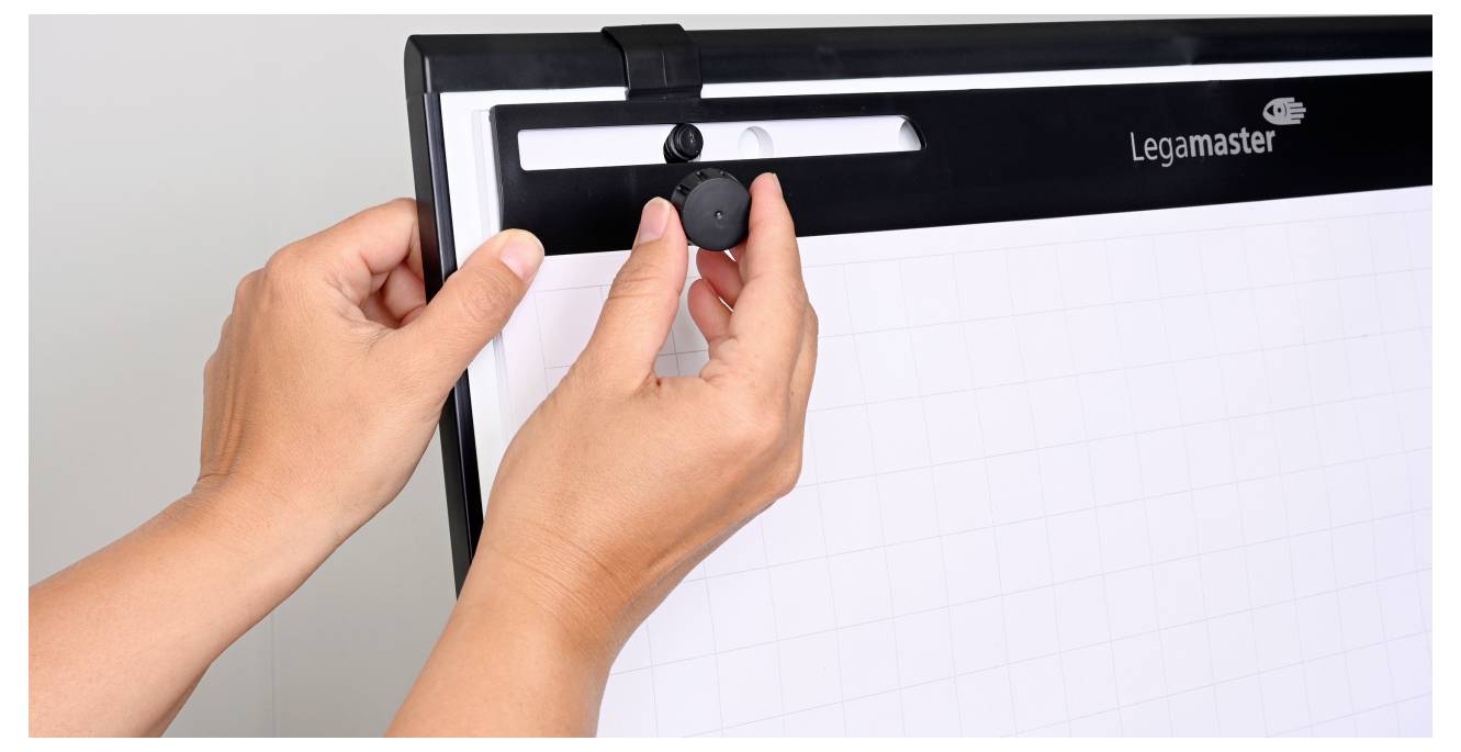 Hände, die einen schwarzen Knopf an einem Legamaster-Flipchart-Ständer justieren und dabei ein Blatt Millimeterpapier befestigen.