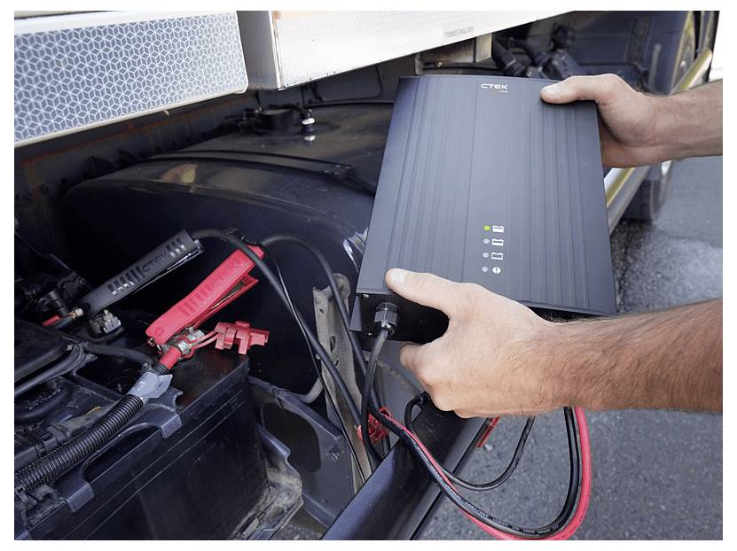 Eine Person schließt ein Cytek-Ladegerät an eine Fahrzeugbatterie an und demonstriert den Ladungsvorgang im Freien.