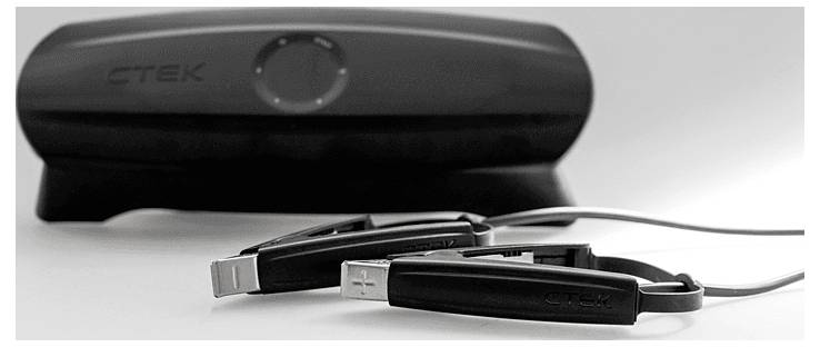 Schwarzer CTEK-Batterielader mit angeschlossenen Klemmen liegt auf einer weißen Oberfläche und betont durch sein Design und seine praktische Funktionalität die Ladeeigenschaften für Fahrzeuge.