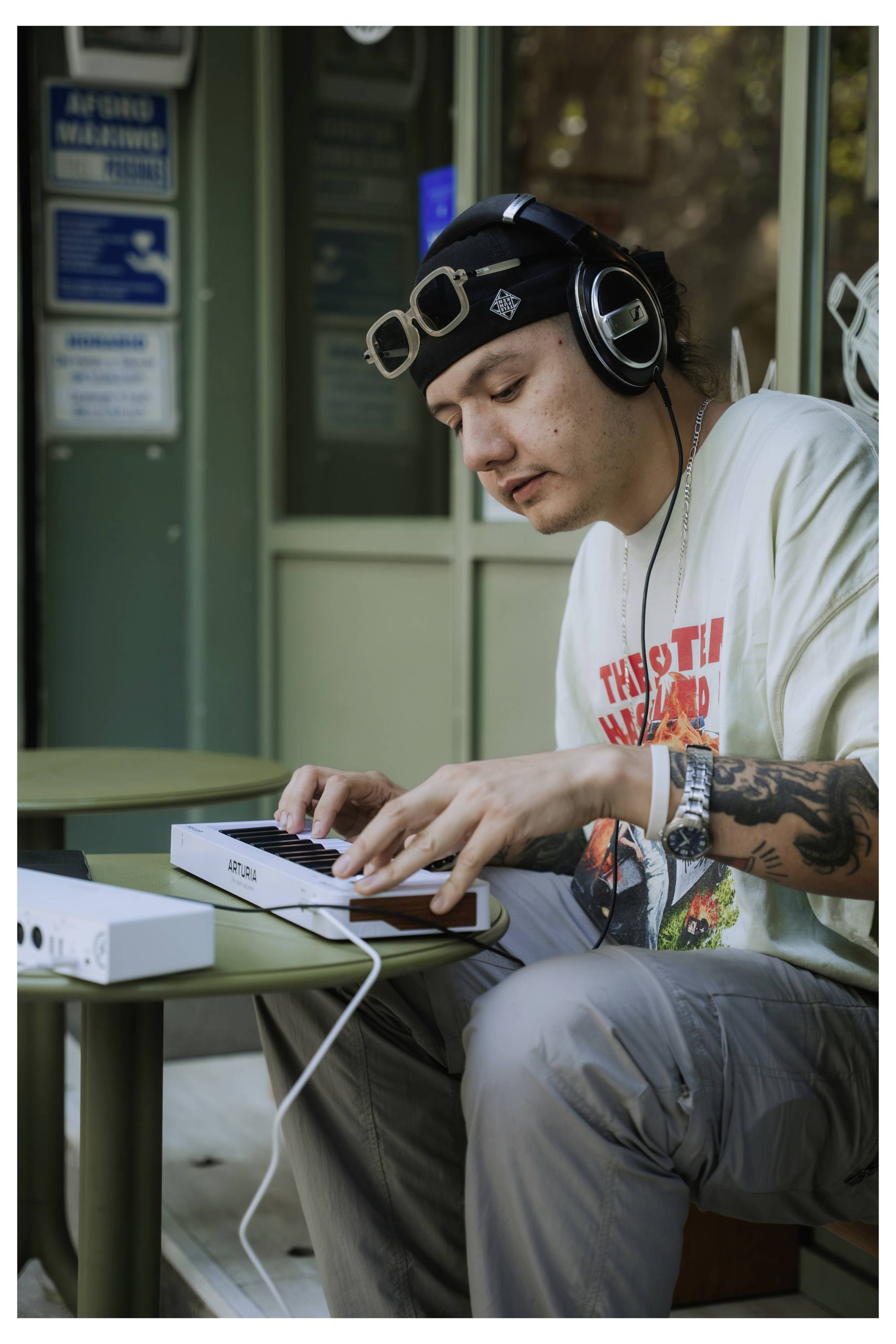 Eine Person mit Kopfhörern und lässiger Kleidung spielt draußen Keyboard. Sie ist konzentriert auf das Instrument und vermittelt den Eindruck, sich dem Musikmachen zu widmen.