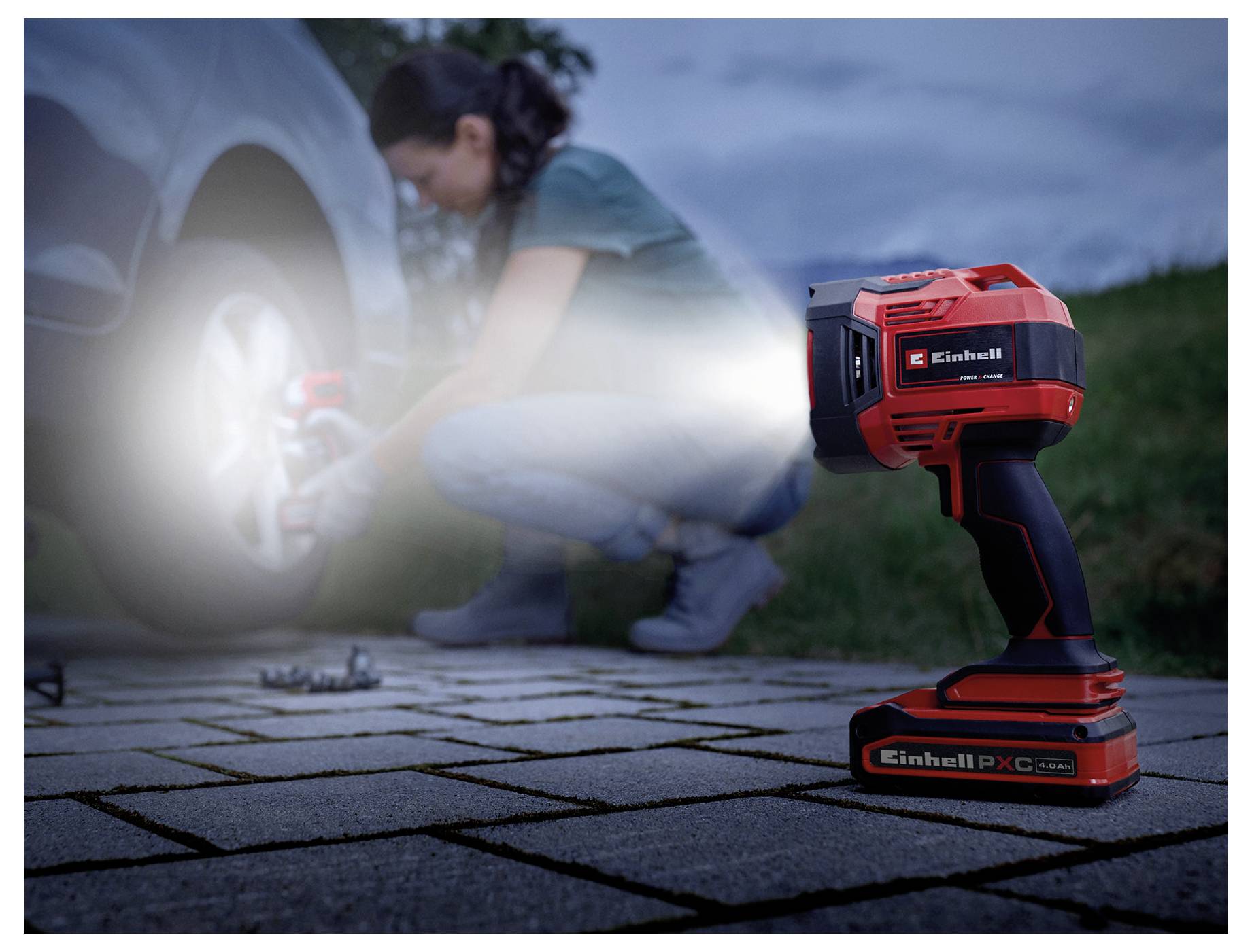 Eine Person, die ein tragbares Elektrowerkzeug benutzt, um ein Autorad auf einer Einfahrt zu befestigen, wobei der Fokus auf dem Werkzeug liegt, das Licht abstrahlt und dessen Verwendung hervorhebt.