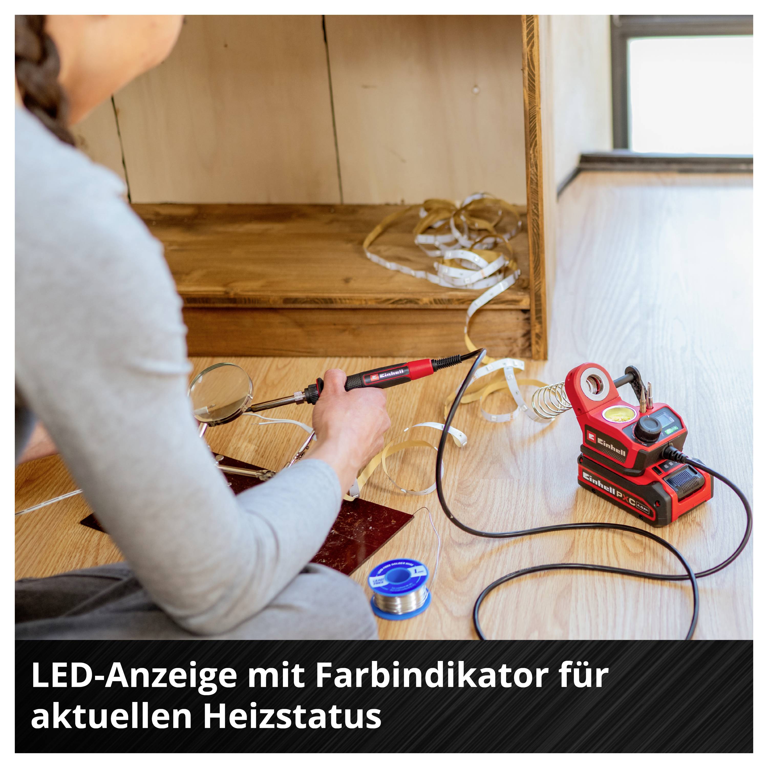 Person sitzt auf dem Boden und arbeitet mit Werkzeug an einem Holzschrank. Elektronisches Gerät und LED-Anzeige zeigen Heizstatus.