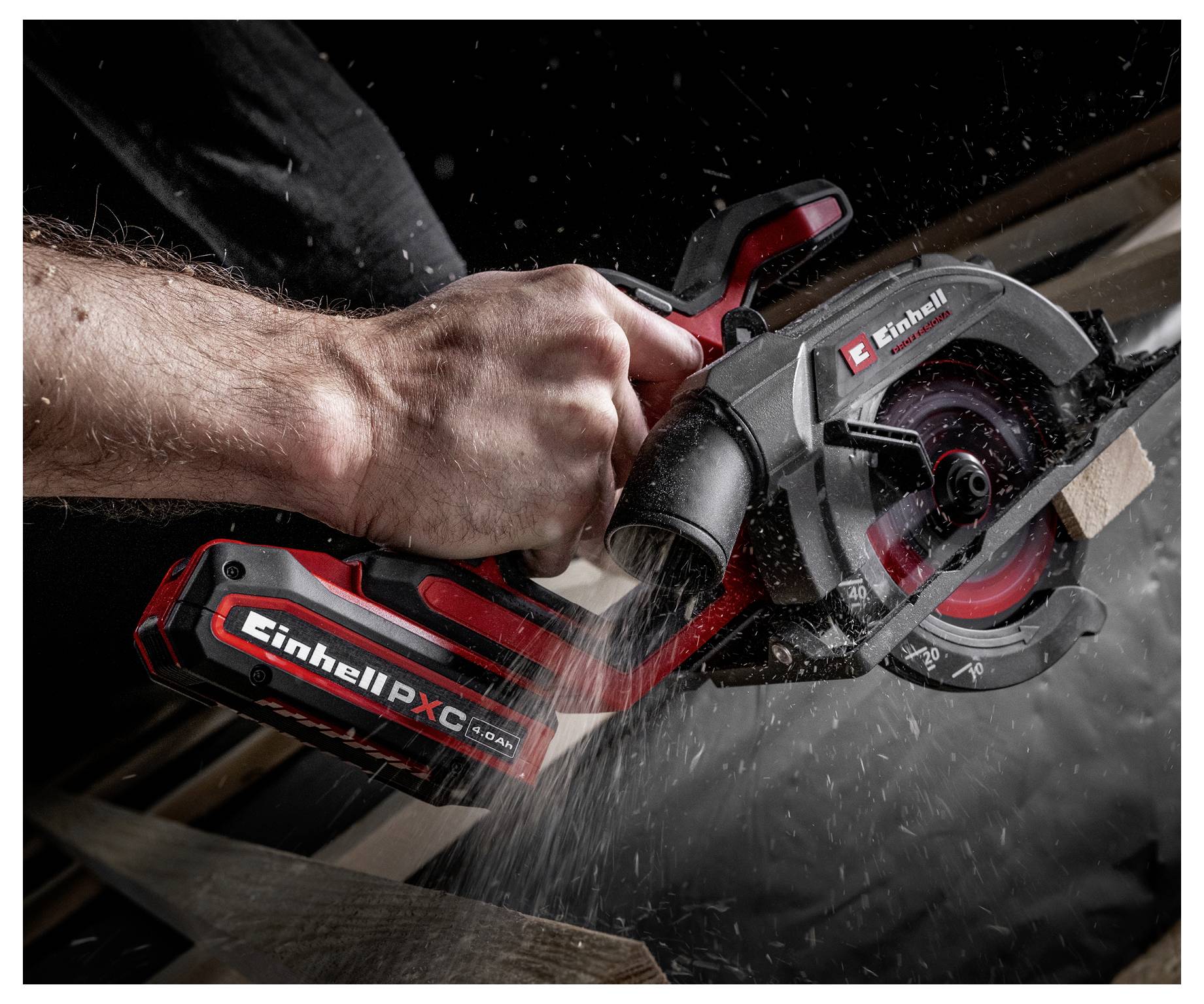 Eine Person verwendet eine rote und schwarze kabellose Kreissäge, um ein Stück Holz zu schneiden, wobei sichtbare Sägespäne entstehen. Die Säge ist mit 'Einhell PX-C' beschriftet.