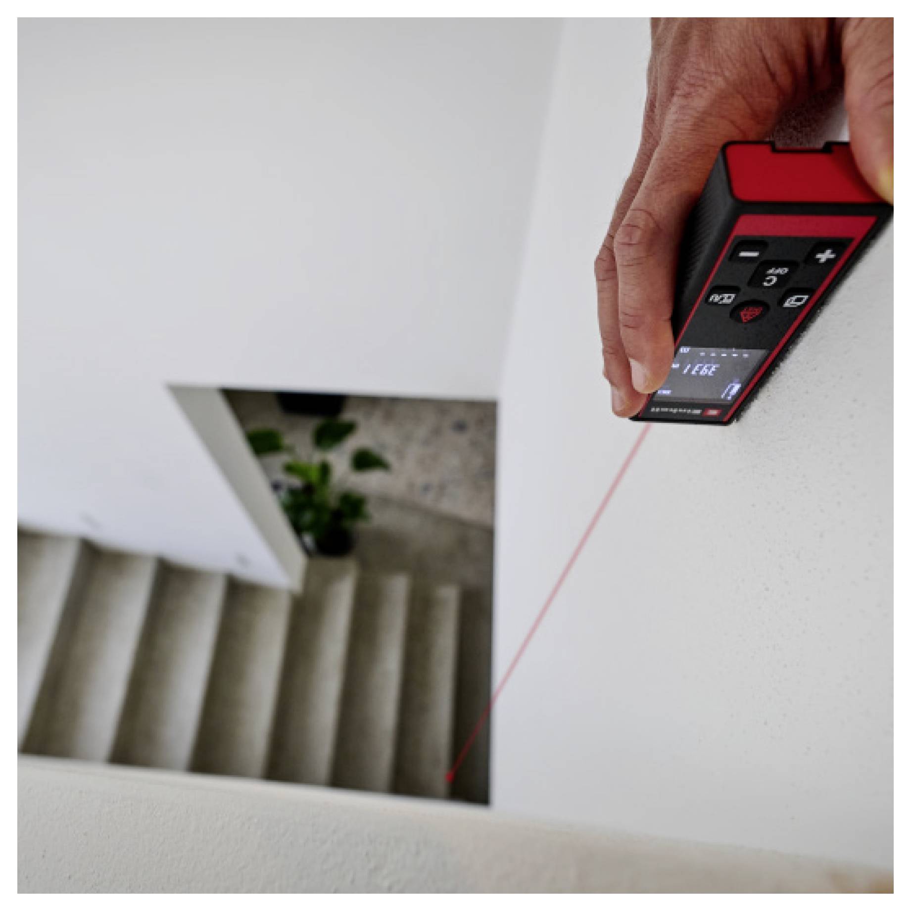 Eine Person verwendet ein rotes digitales Laser-Entfernungsmessgerät, um einen vertikalen Abfall neben einer Treppe zu vermessen.
