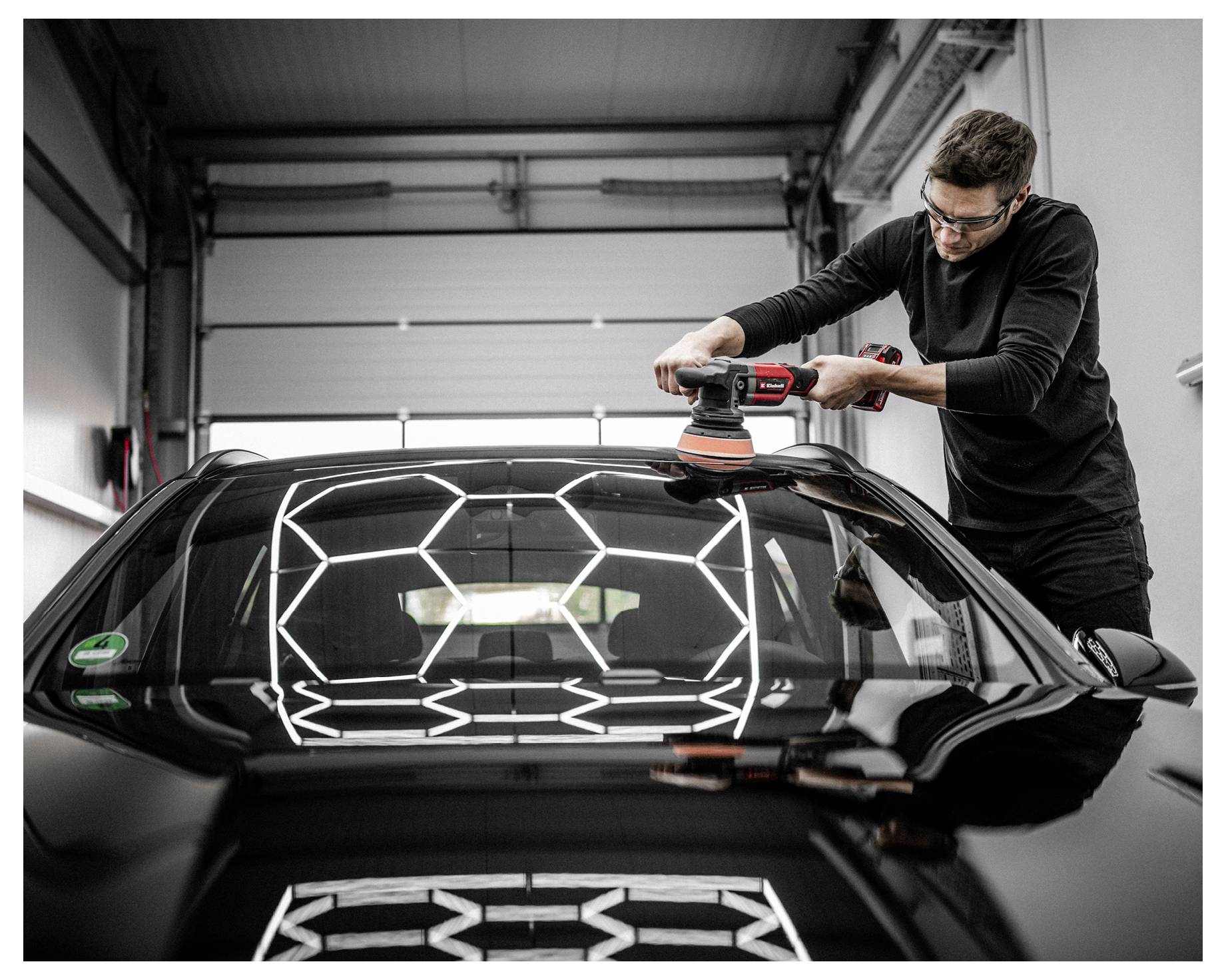 Eine Person poliert das Dach eines schwarzen Autos in einer Garage und reflektiert helle sechseckige Lichter, was einen glänzenden Finish betont.