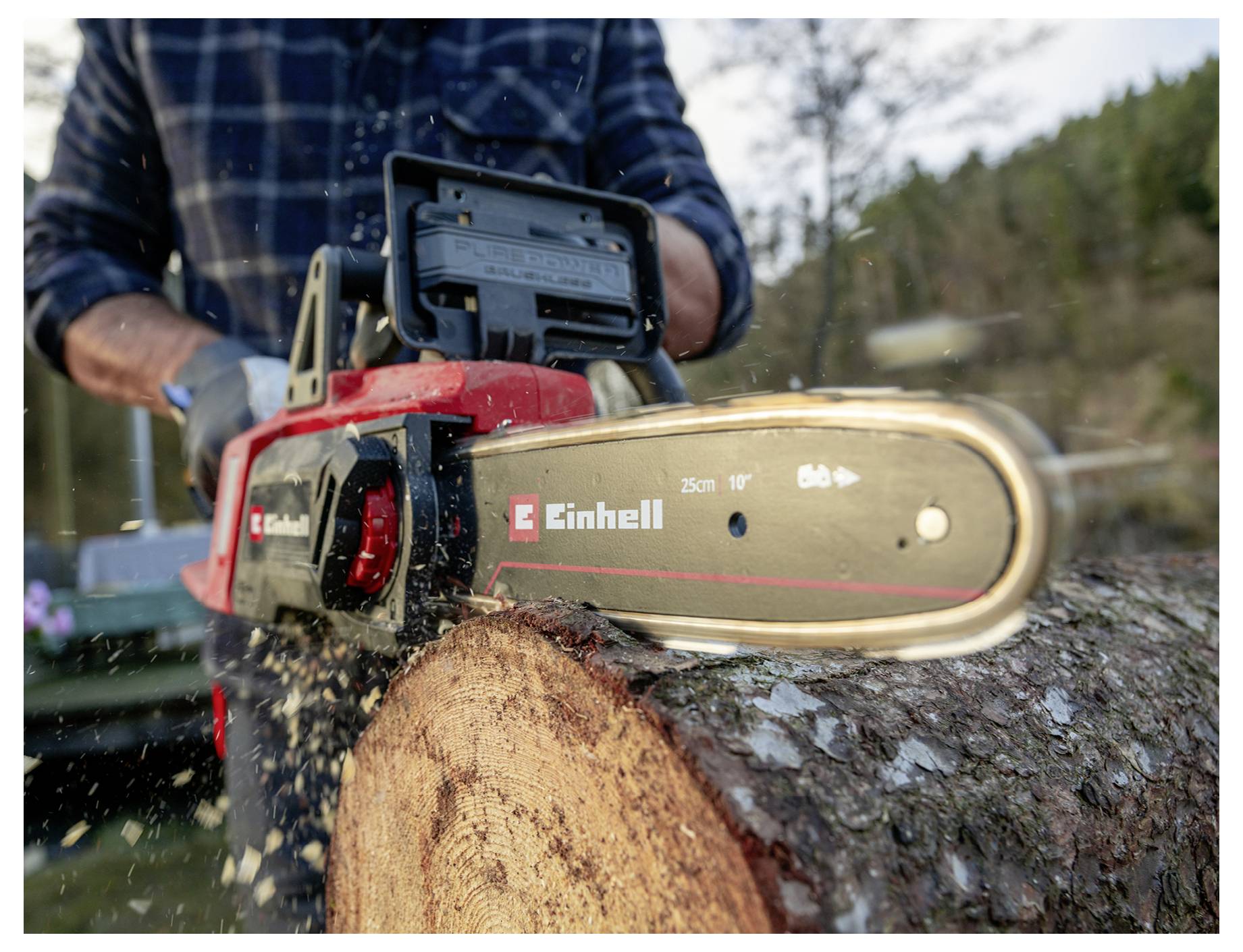 Eine Person in Flanell verwendet eine rote Motorsäge, um einen großen Baumstamm im Freien zu zersägen, während Holzspäne durch die Luft wirbeln.