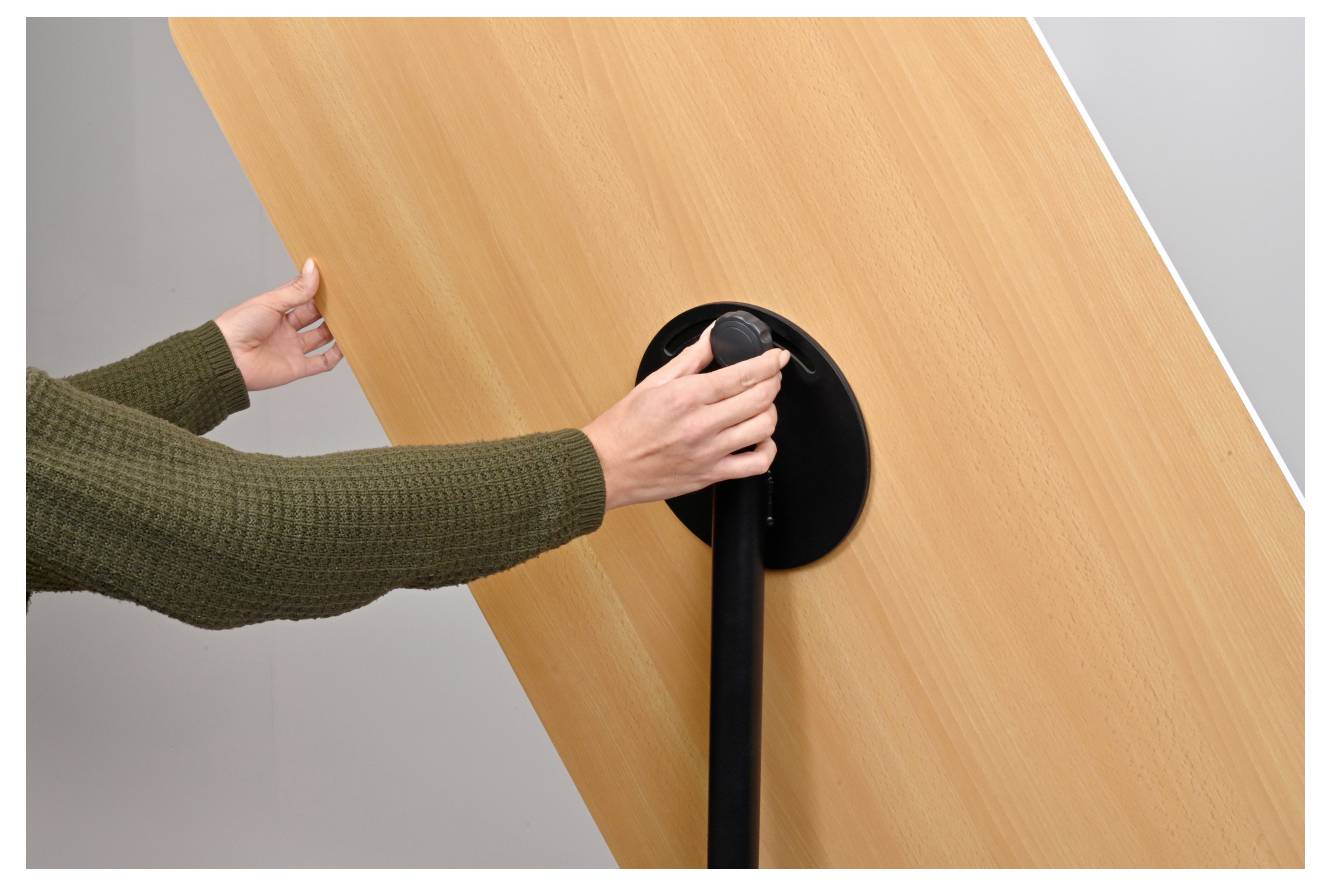 Eine Person in einem grünen Pullover bedient eine Handkurbel an einem großen Holzpaneel und verändert möglicherweise dessen Position oder Winkel.