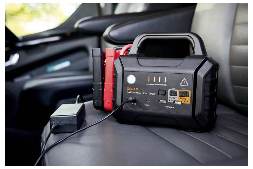 Ein tragbares Autobatterieladegerät mit Starthilfekabeln liegt auf einem Autositz, einsatzbereit.