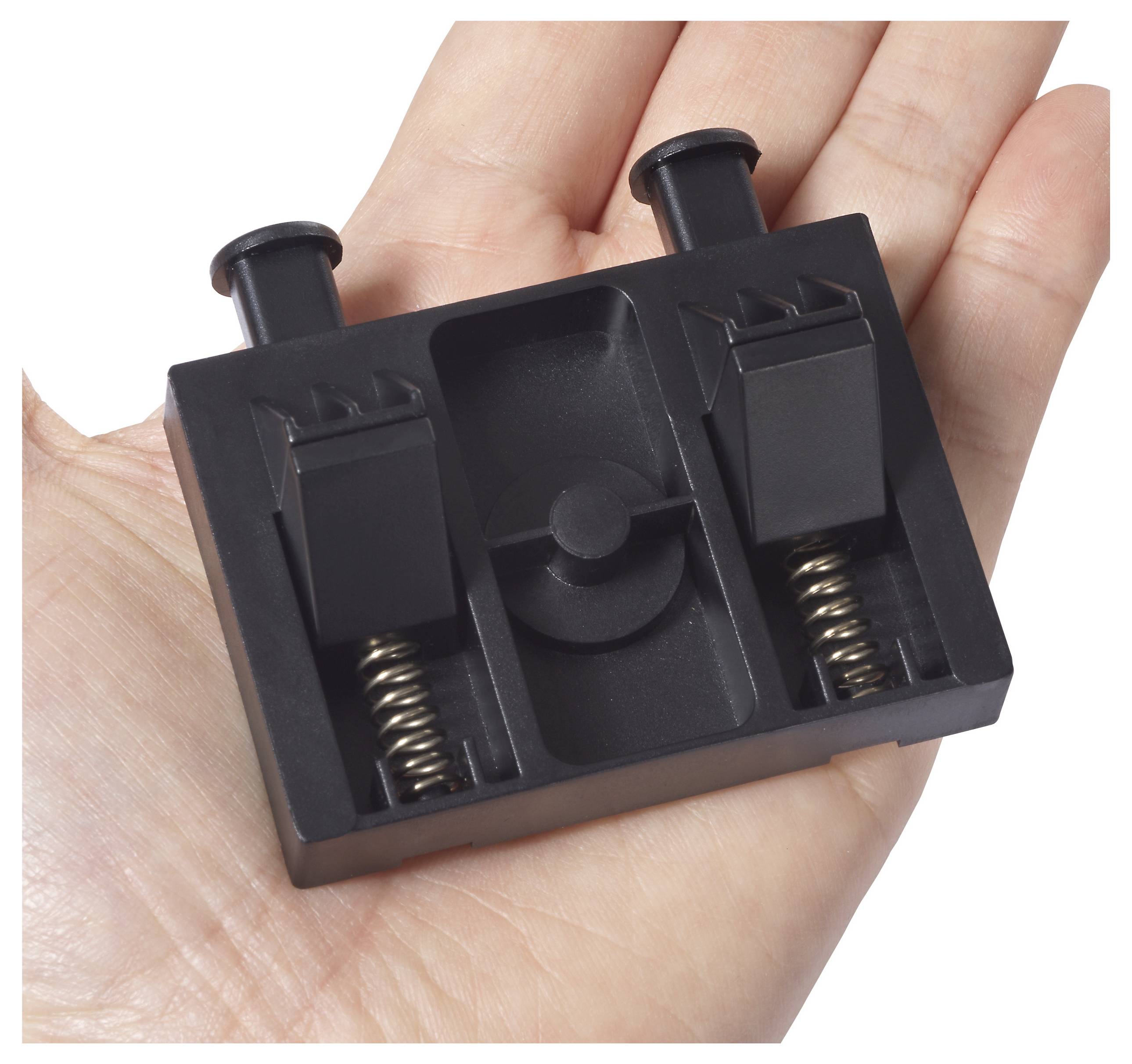Eine Hand hält ein kleines schwarzes Kunststoffteil mit zwei Federn und Kerben, möglicherweise ein Teil einer mechanischen oder elektronischen Vorrichtung.