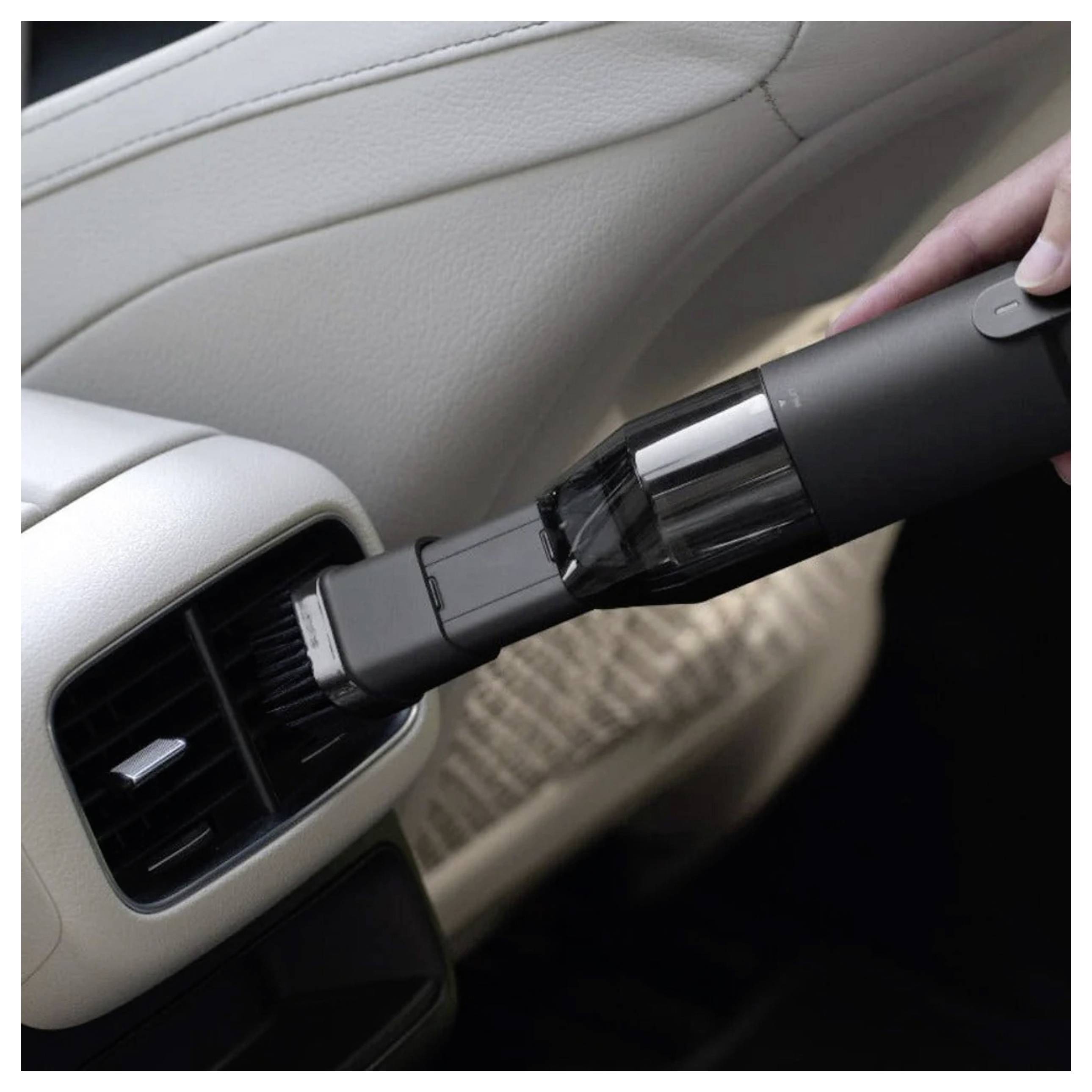 Eine Hand, die einen tragbaren Staubsauger verwendet, um die Lüftungsschlitze eines Autos zu reinigen und dabei den Fokus auf eine effiziente Innenreinigung des Fahrzeugs legt.