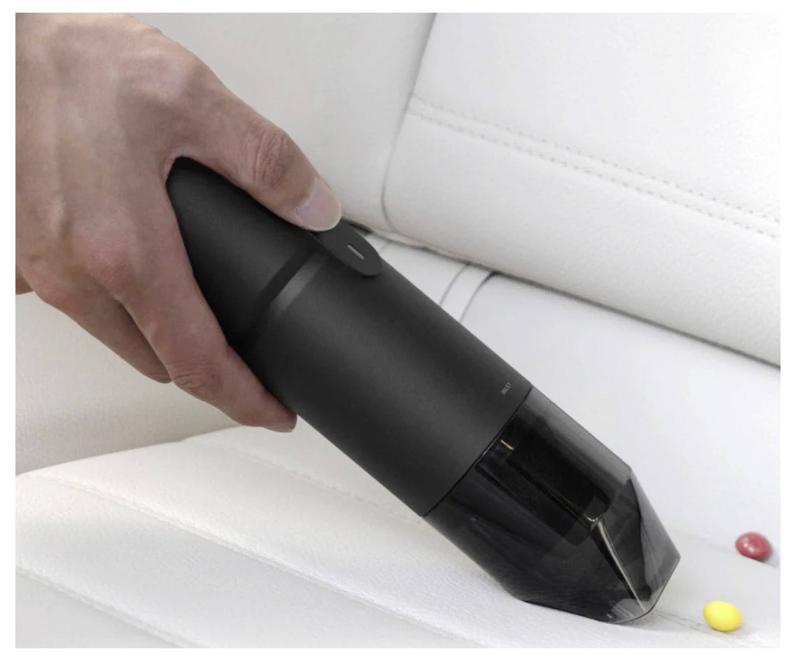 Eine Hand hält einen kleinen schwarzen tragbaren Staubsauger und reinigt Süßigkeitenreste von einem weißen Sofa und demonstriert dabei Benutzerfreundlichkeit und Mobilität.