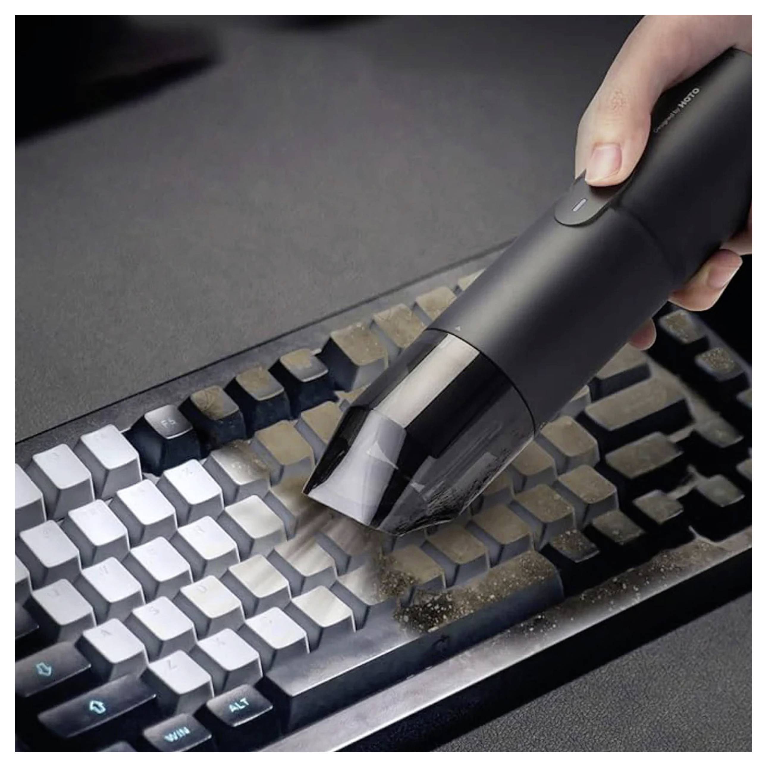 Eine Hand benutzt einen kompakten Staubsauger, um Staub und Schmutz von einer Tastatur zu entfernen und veranschaulicht dabei einen Reinigungsprozess.