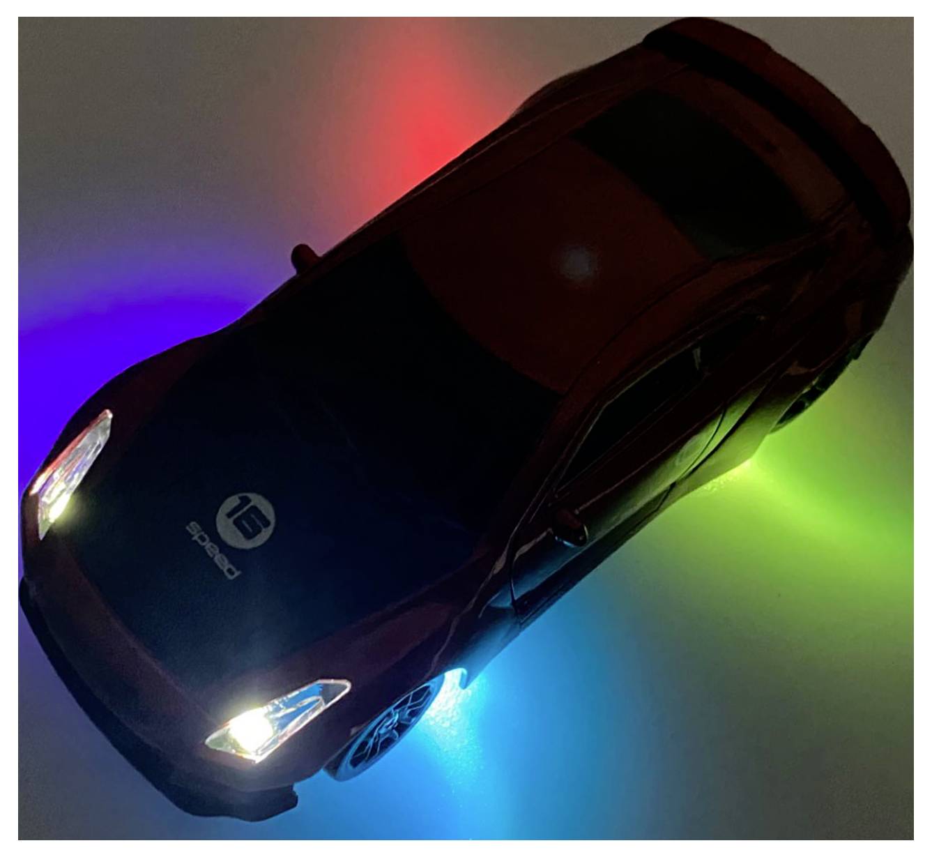 Ein Spielzeugauto mit leuchtenden Scheinwerfern und bunten LED-Lichtern darunter, die einen Halo-Effekt auf der Oberfläche in Rot, Blau und Grün erzeugen.