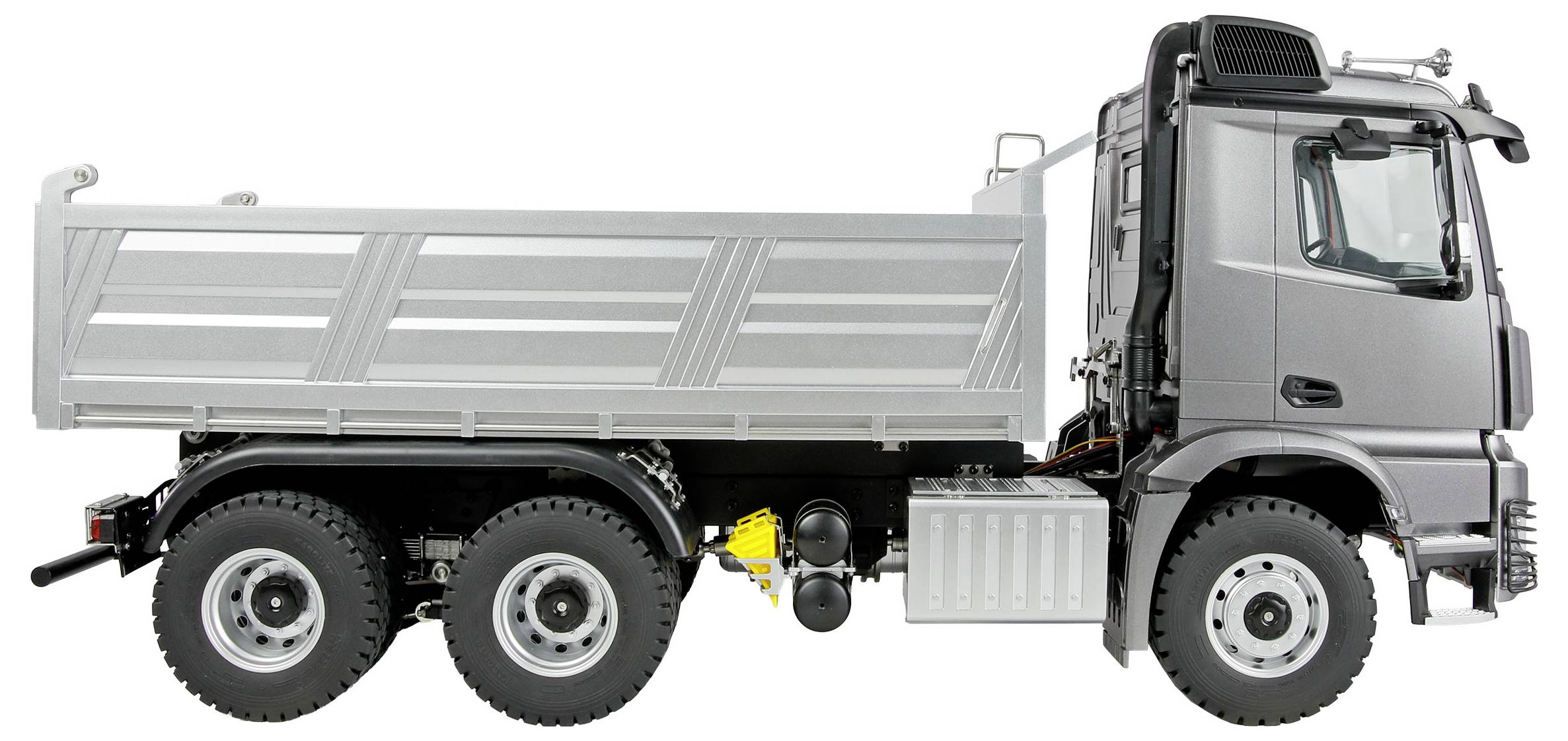 Ein grauer Kipper mit sechs Rädern ist geparkt und zeigt sein Seitenprofil mit einer leeren Ladefläche und sichtbaren Details der Fahrerkabine und der Reifen.