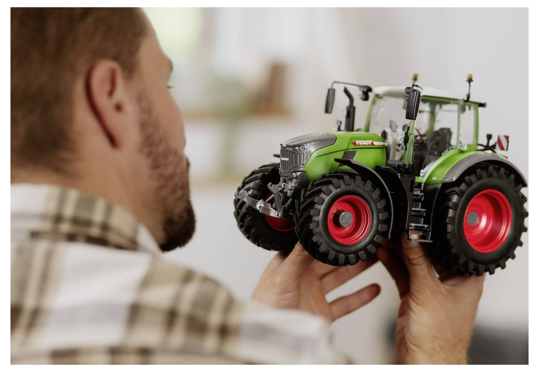 Ein Mann hält ein detailliertes Modell eines grünen und roten Traktors und untersucht dessen Merkmale genau.
