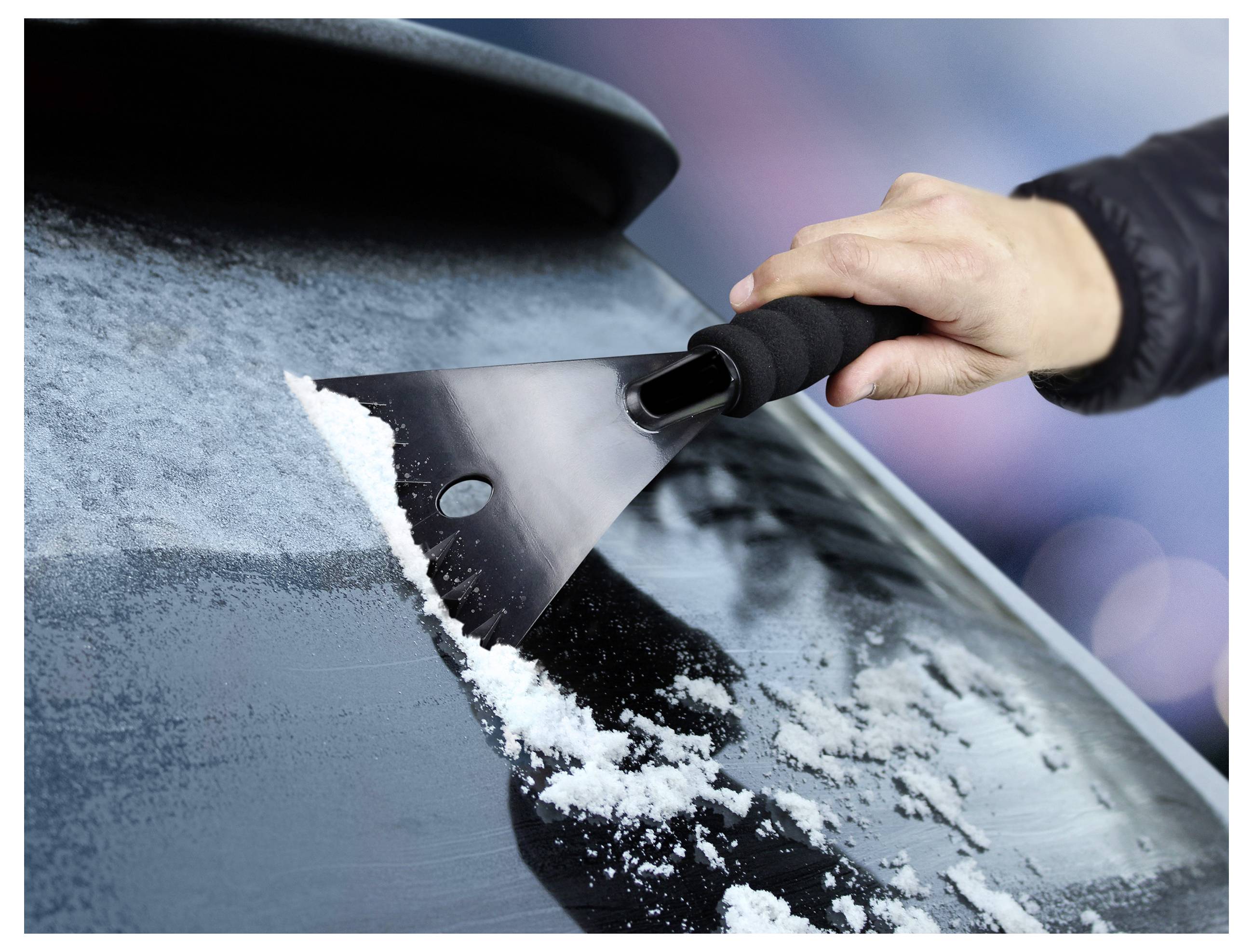 Eine Hand einer Person benutzt einen Eiskratzer, um Eis und Schnee von einer Autoscheibe an einem kalten Tag zu entfernen.