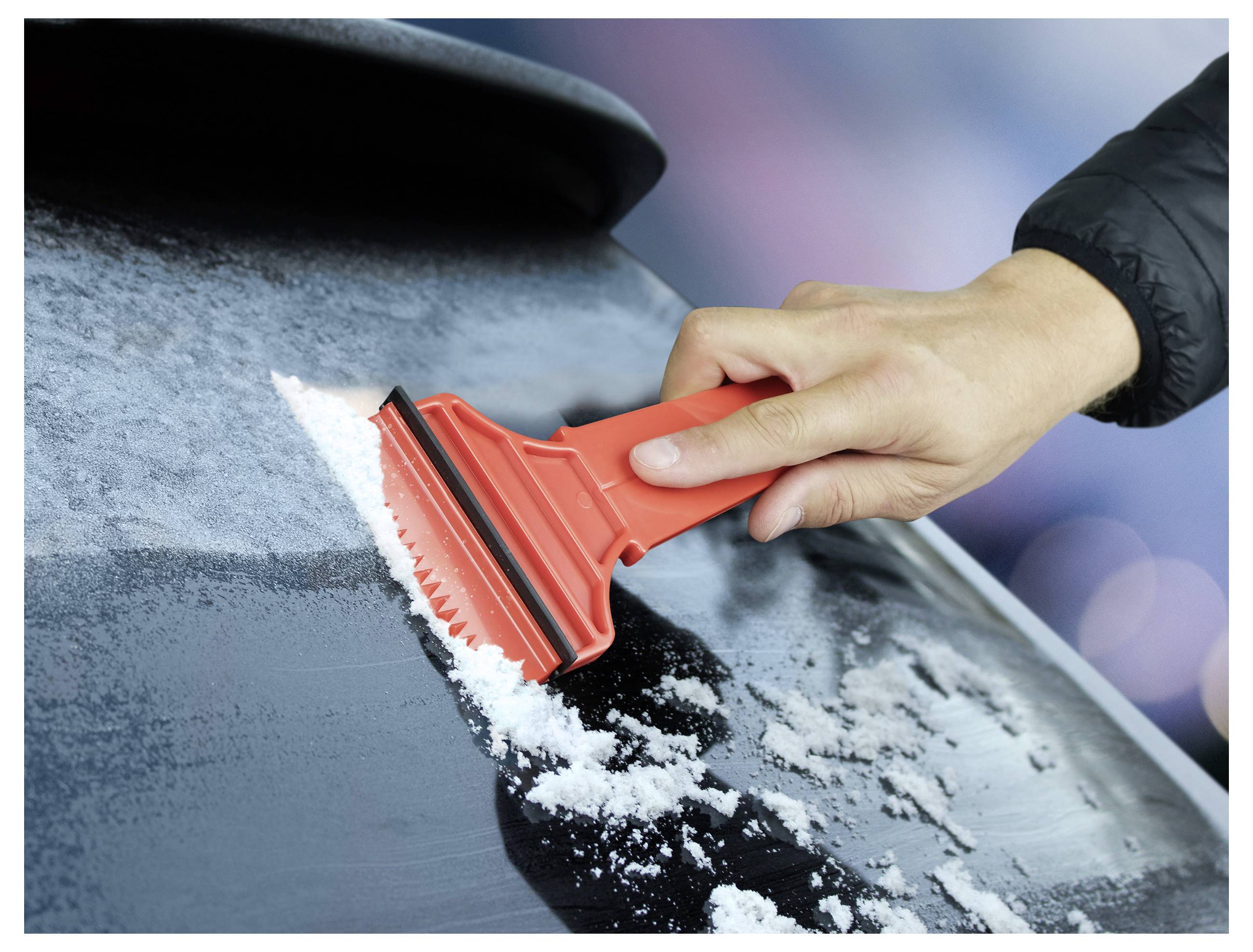Eine Person verwendet einen roten Eiskratzer, um Schnee und Eis von der Windschutzscheibe eines Autos an einem kalten Tag zu entfernen.