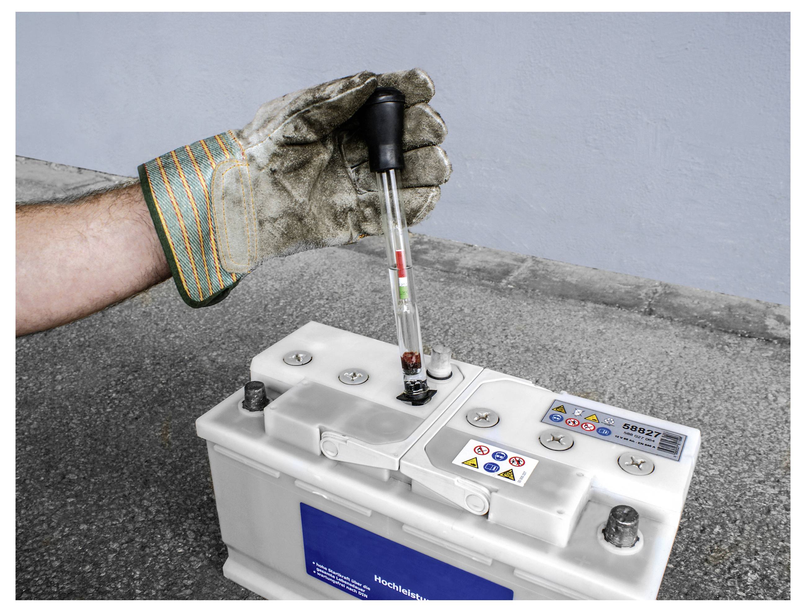 Eine behandschuhte Hand testet eine Autobatterie mit einem Aräometer. Das Aräometer zeigt Flüssigkeit an, die den Zustand der Batterie anzeigt.