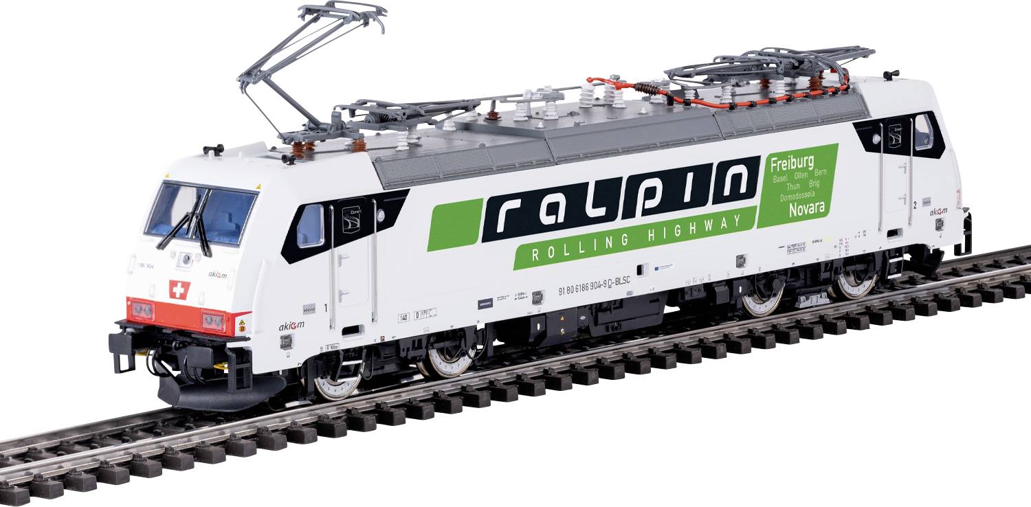 Ein weißer Zug mit dem Logo 'ralpin' und 'ROLLING HIGHWAY' an der Seite fährt auf Schienen. Schilder zeigen die Strecke 'Freiburg - Novara'.